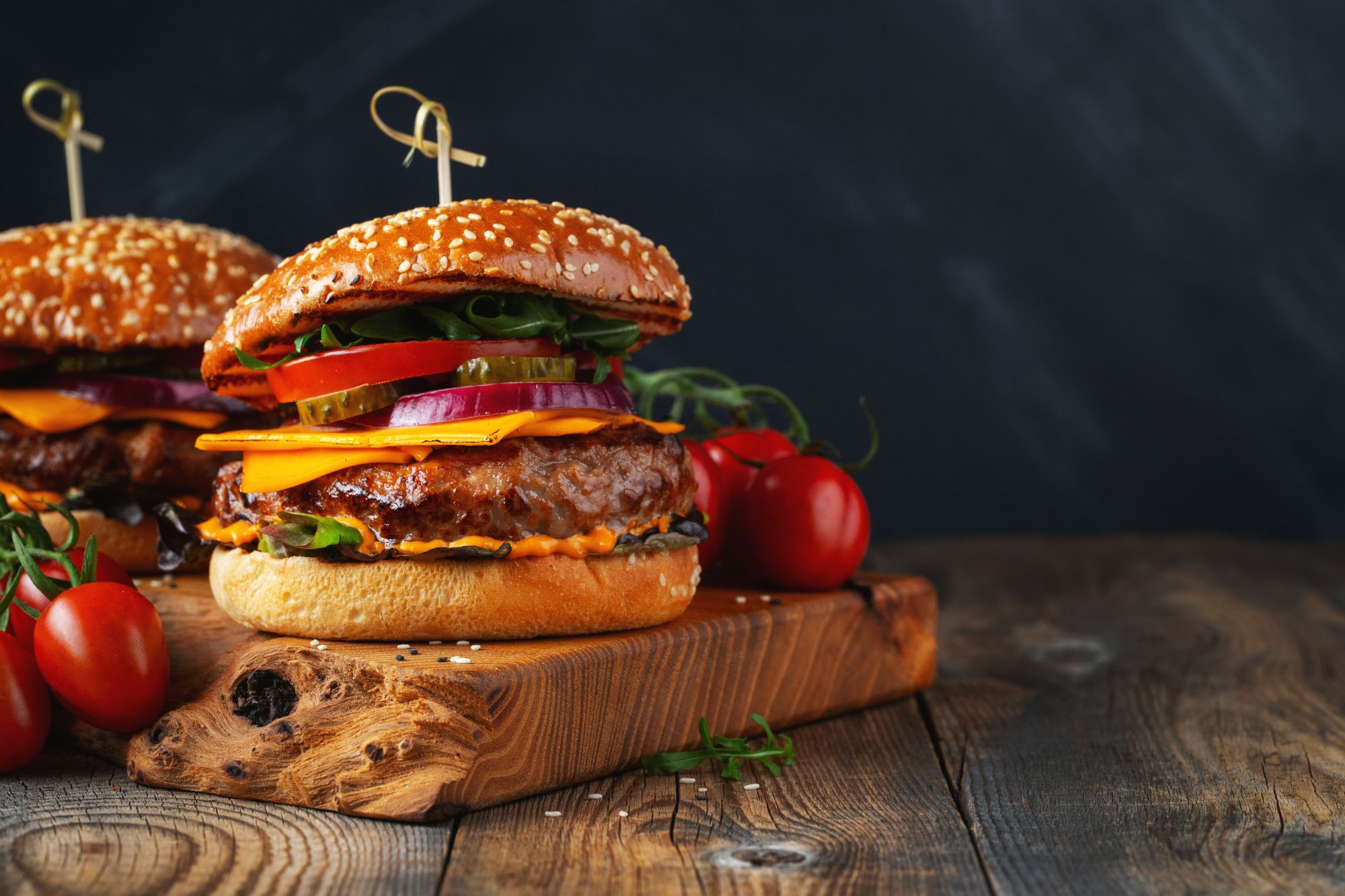Soczysty hamburger z serem, warzywami i pomidorami na drewnianym desce, na tle ciemnego tła.