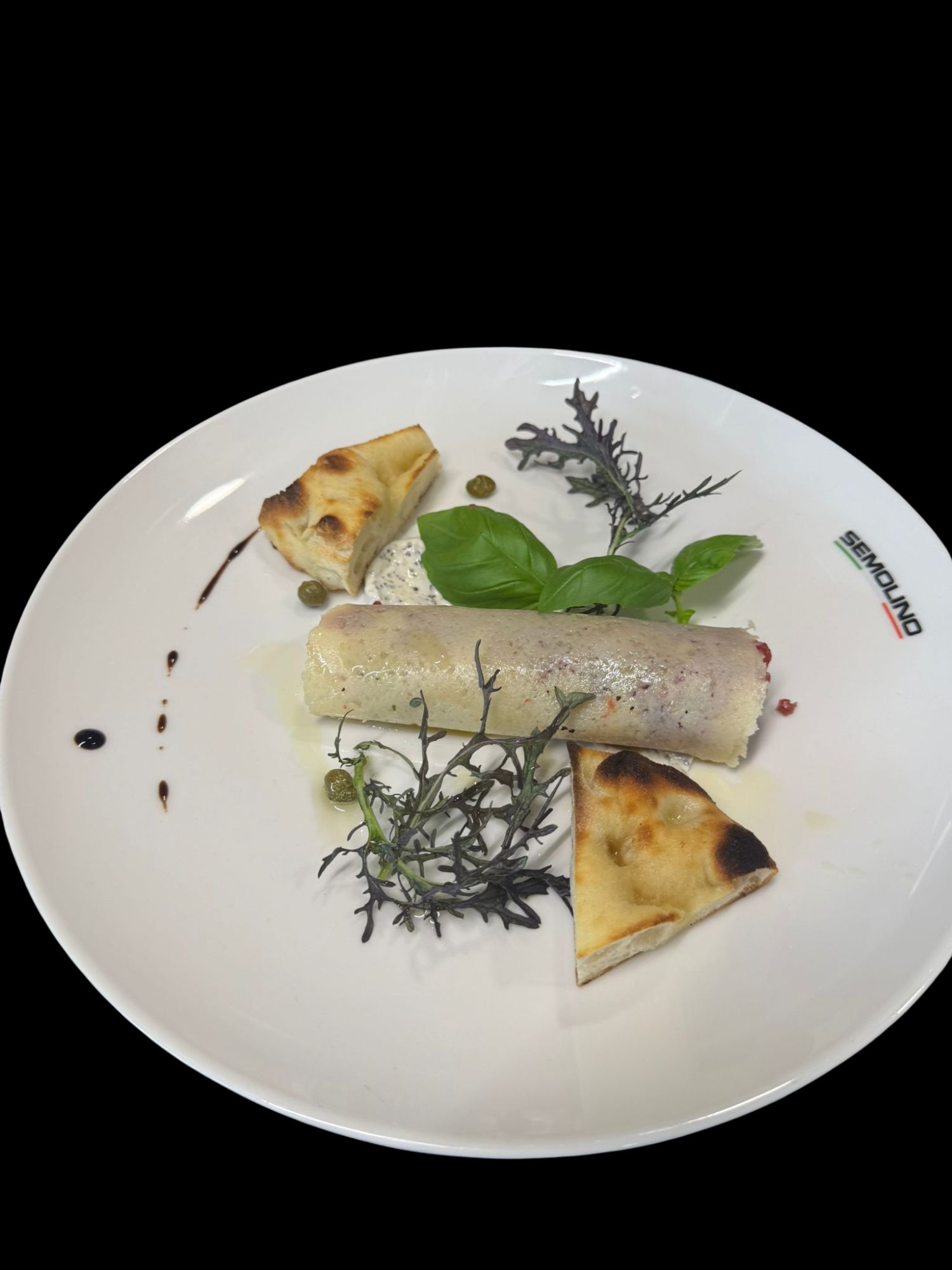 Danie gastronomiczne: zrolowane mięso z ziołami, podane z grillowanym chlebem i dekoracjami z sosu.