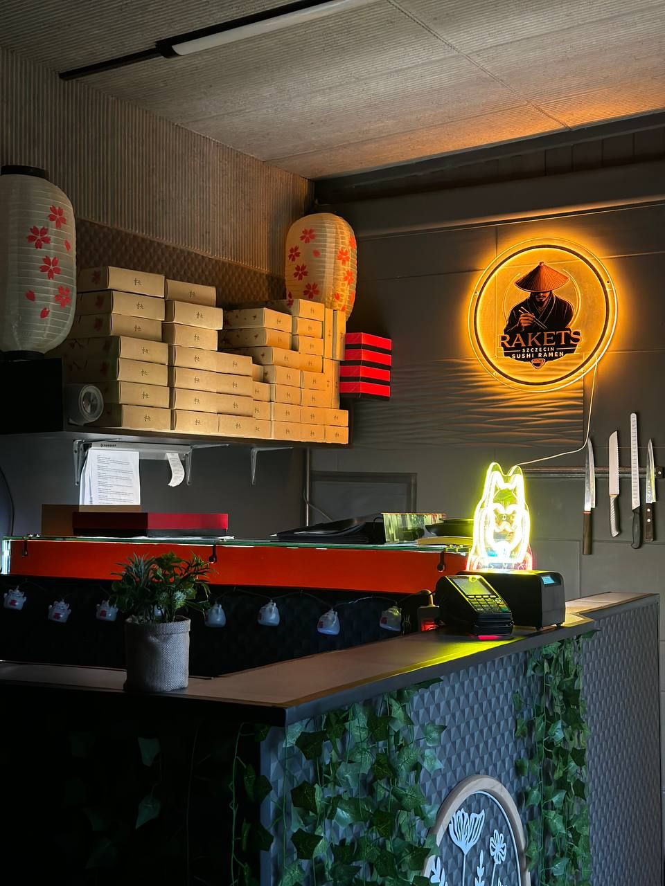 Wnętrze restauracji azjatyckiej z neonem, lampionami i drewnianymi skrzynkami do przechowywania.