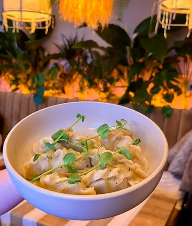 Kremowe pierogi w misce z mikro ziołami, w tle roślinność i lampy w stylu boho.