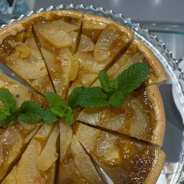 Tarta z jabłkami pokrojona w kawałki, udekorowana świeżą miętą, serwowana na szklanym talerzu.