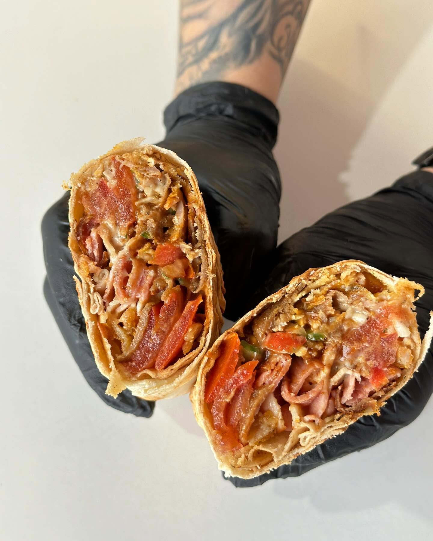 Osoba w czarnych rękawiczkach trzyma przekrojone burrito z mięsem, papryką i przyprawami.