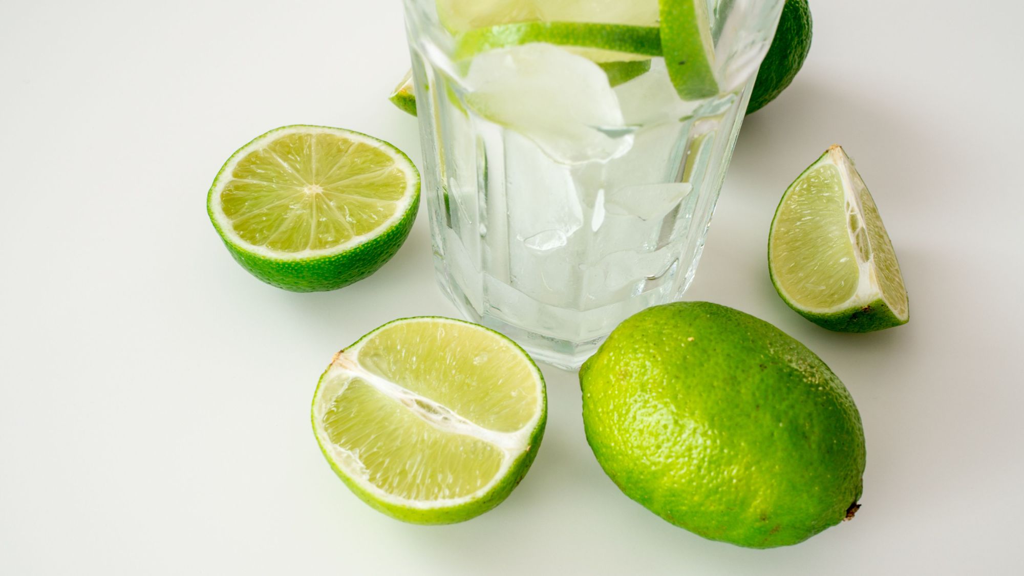 Szklanka lodu z plasterkami limonki i pokrojonymi limonkami na białym tle.