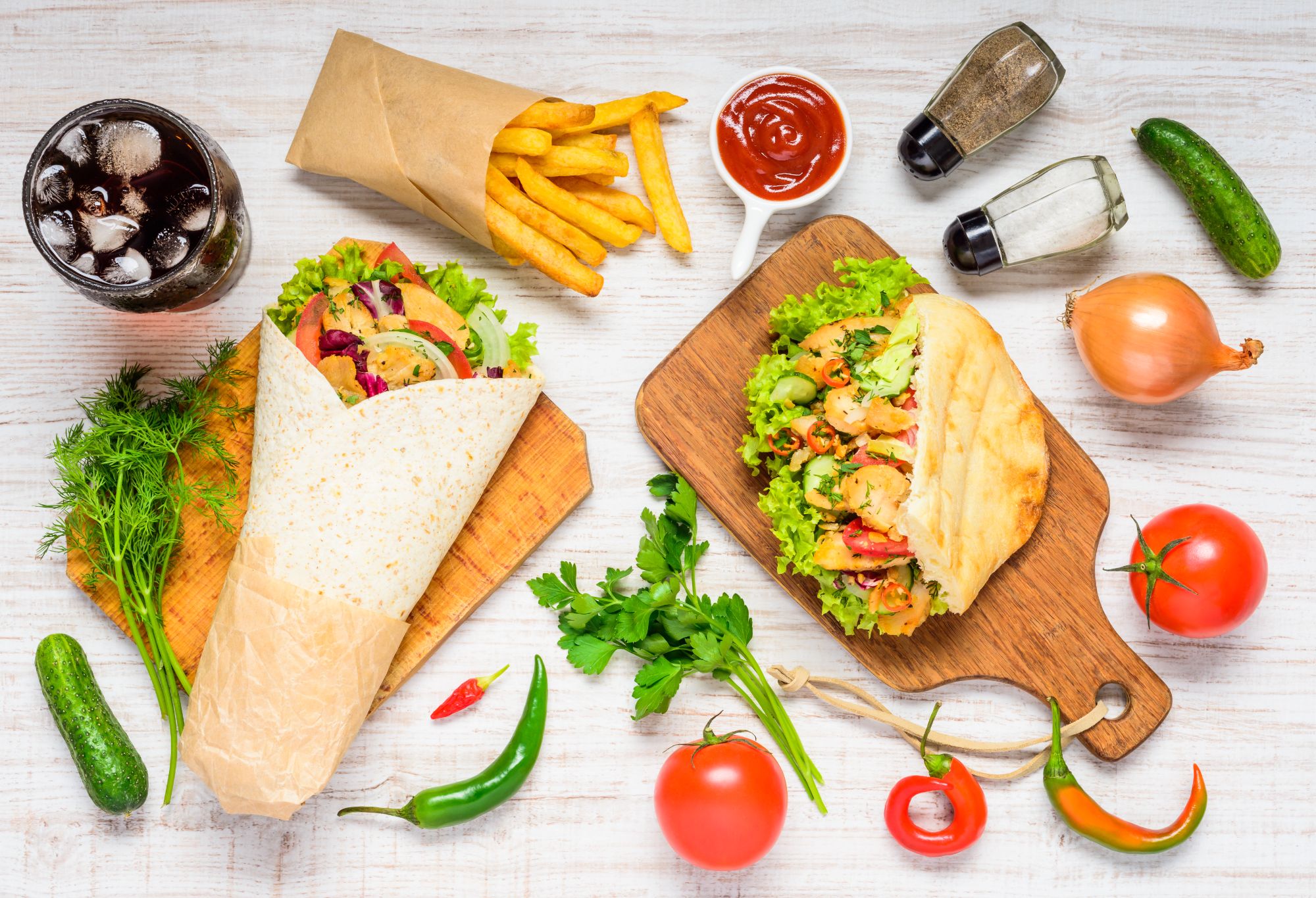 Jedzenie typu fast food: tortilla z warzywami i kurczakiem, chleb pita, frytki, sos, napój i świeże składniki.
