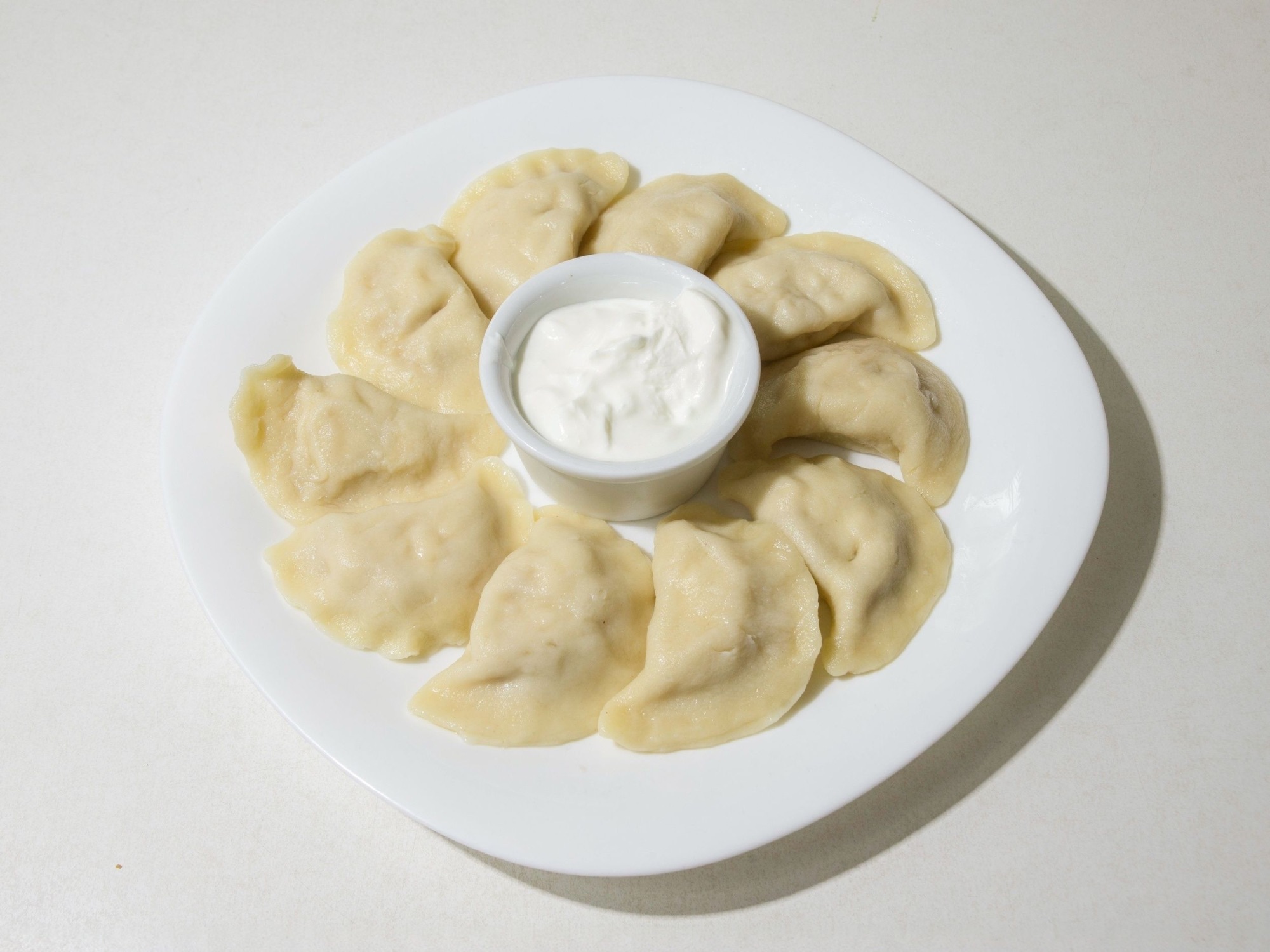 Pierogi na talerzu z sosem śmietanowym w białej miseczce w centrum.