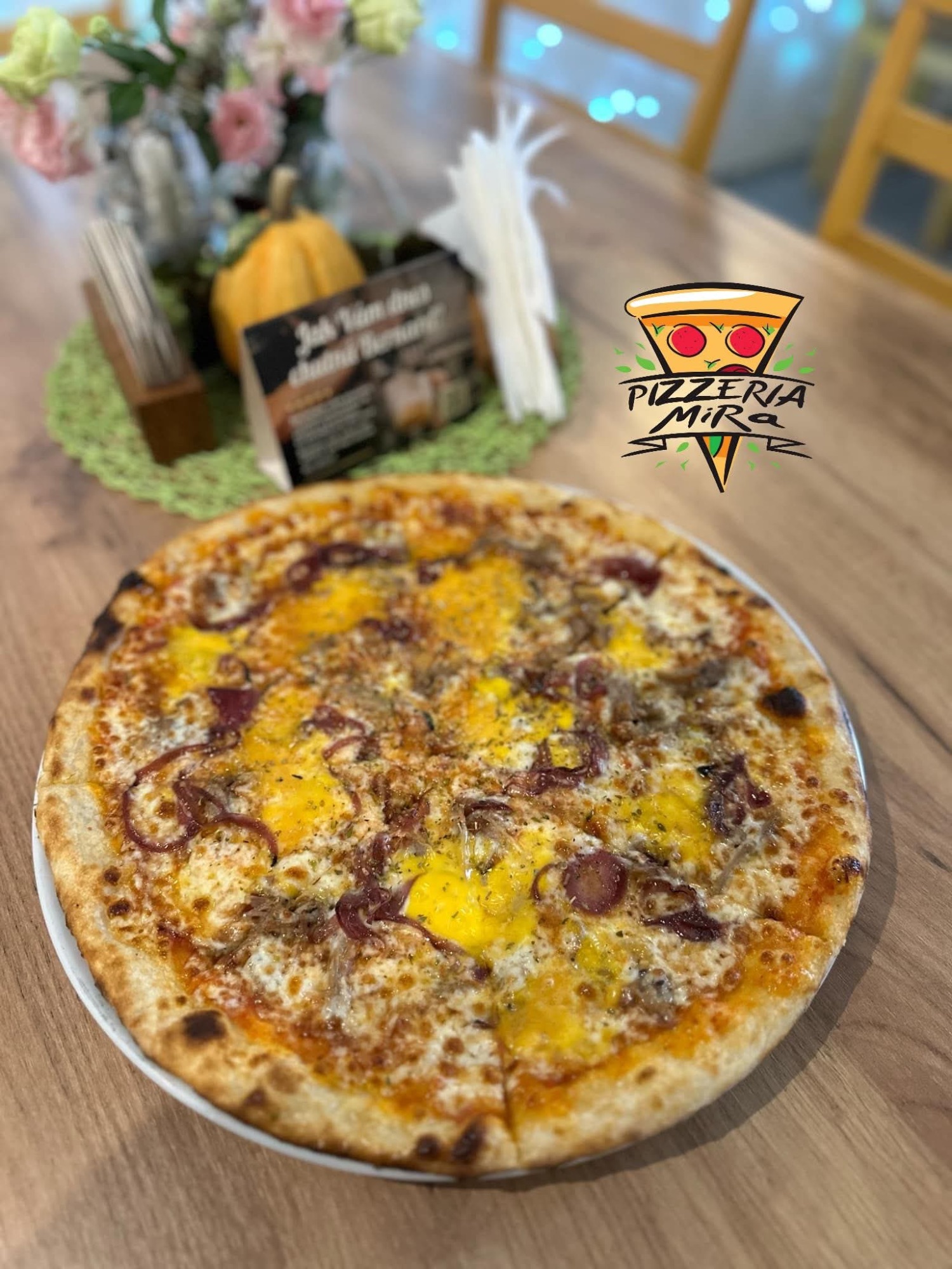 Pizza s mletým mäsom, cibuľou a syrom, servírovaná v pizzerii MIRA, na drevenom stole.