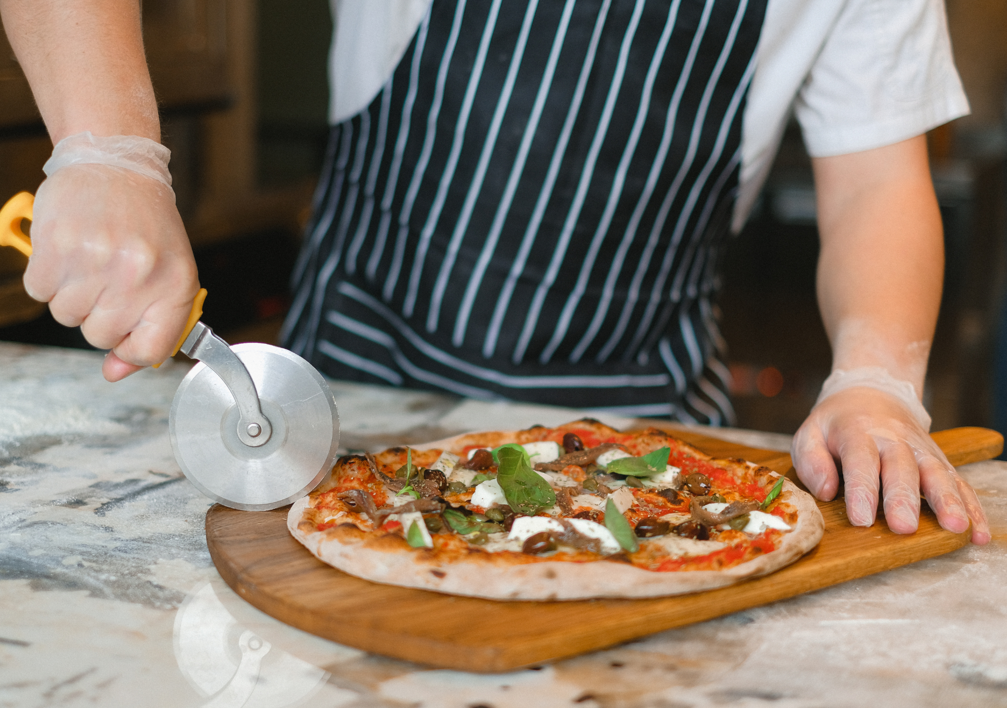 Kuchár krája čerstvú pizzu na drevenej doske s pizze a ortofónom na pizzu.