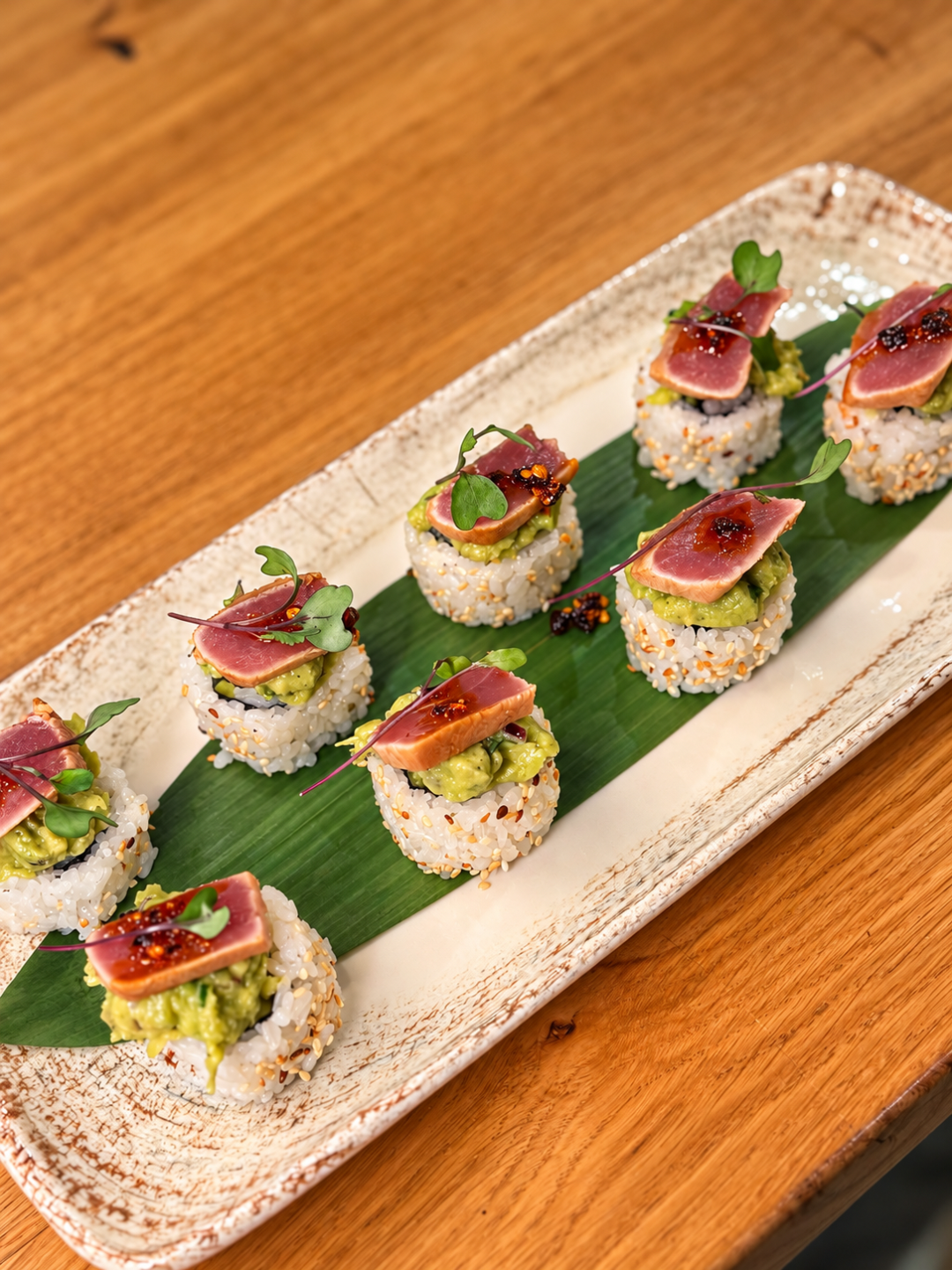 Talerz sushi z ryżem, awokado i kawałkami surowej ryby, podany na liściu bananowca.