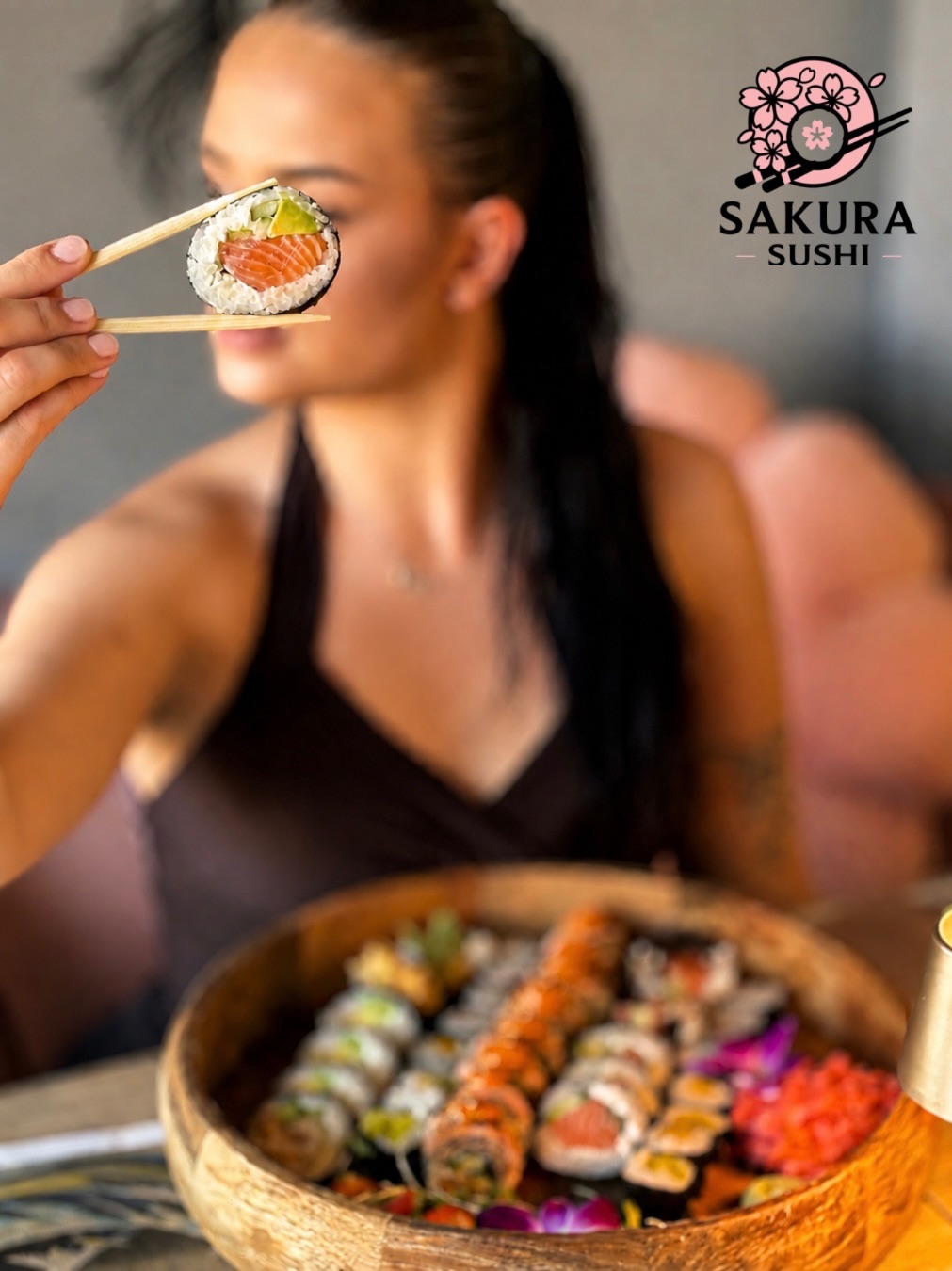 Kobieta trzymająca sushi w pałeczkach, na stole różnorodne rolki sushi, logo Sakura Sushi w rogu.