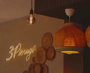Ściana w restauracji z napisem "3 Pierogi" i dekoracyjnymi talerzami oraz wiszącymi lampami.