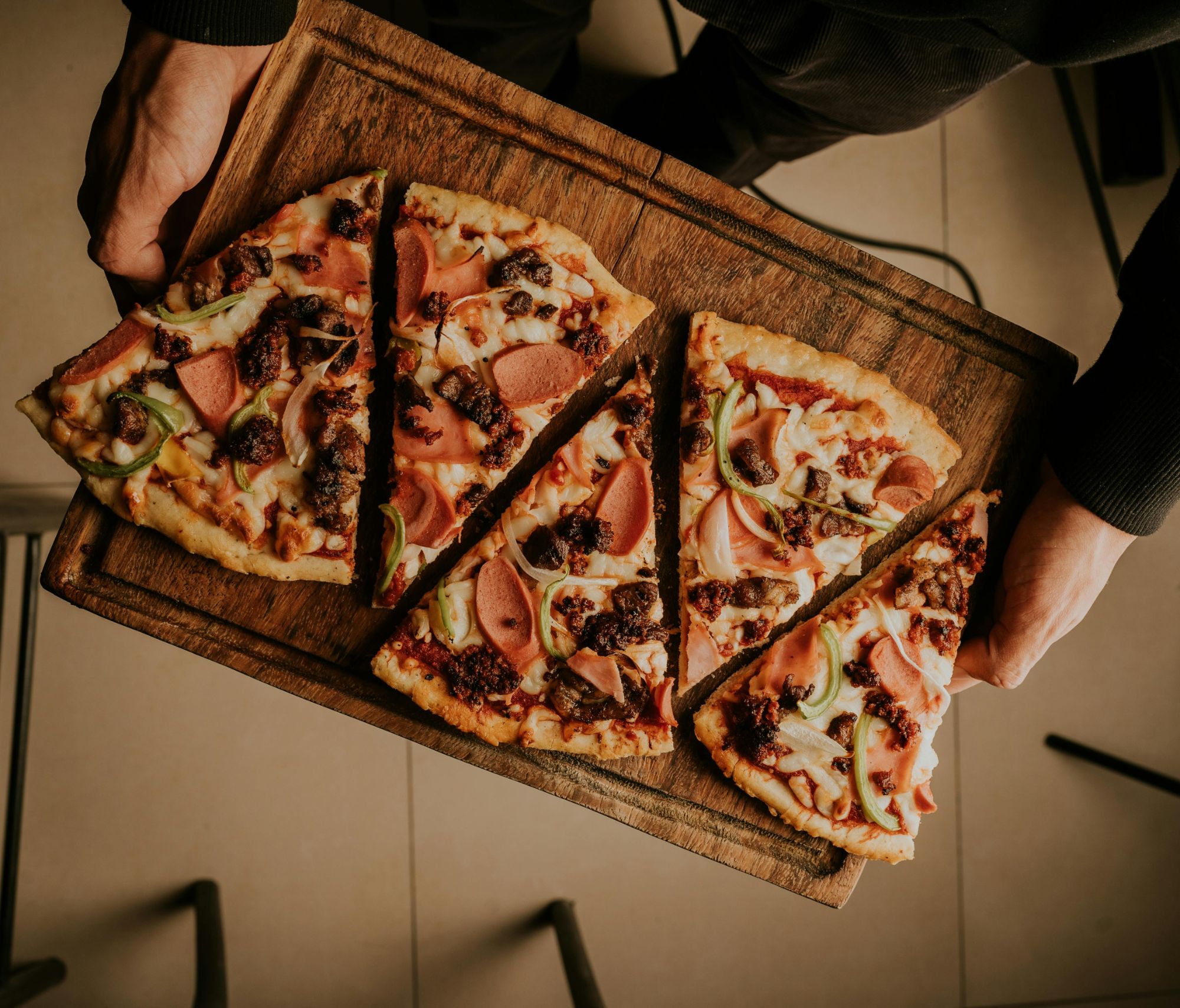 Osoba trzymająca tacę z pięcioma kawałkami pizzy na drewnianej desce.