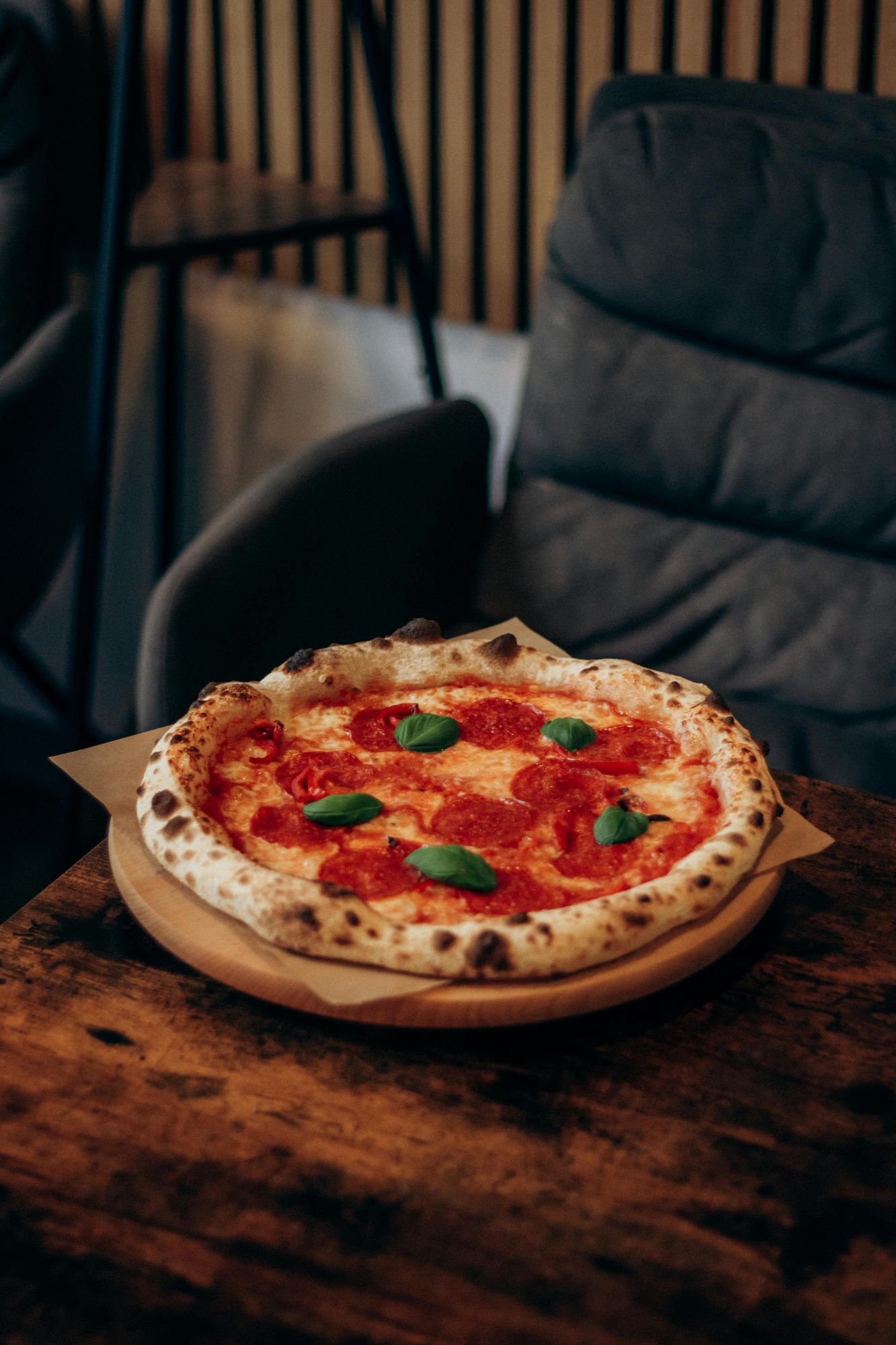 Pizza pepperoni z bazylią na drewnianej desce na tle nowoczesnej kawiarni.