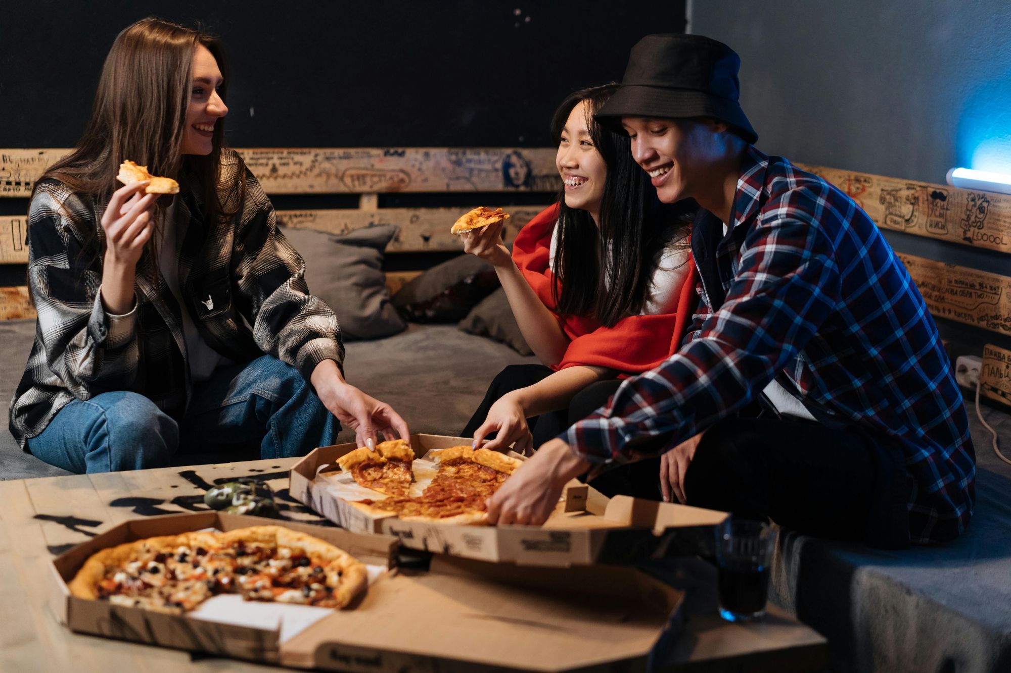 Trzej przyjaciele jedzą pizzę na kanapie w przytulnym otoczeniu, ciesząc się wspólnym czasem.