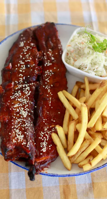 Soczyste żeberka w sosie BBQ, frytki i sałatka coleslaw na talerzu.