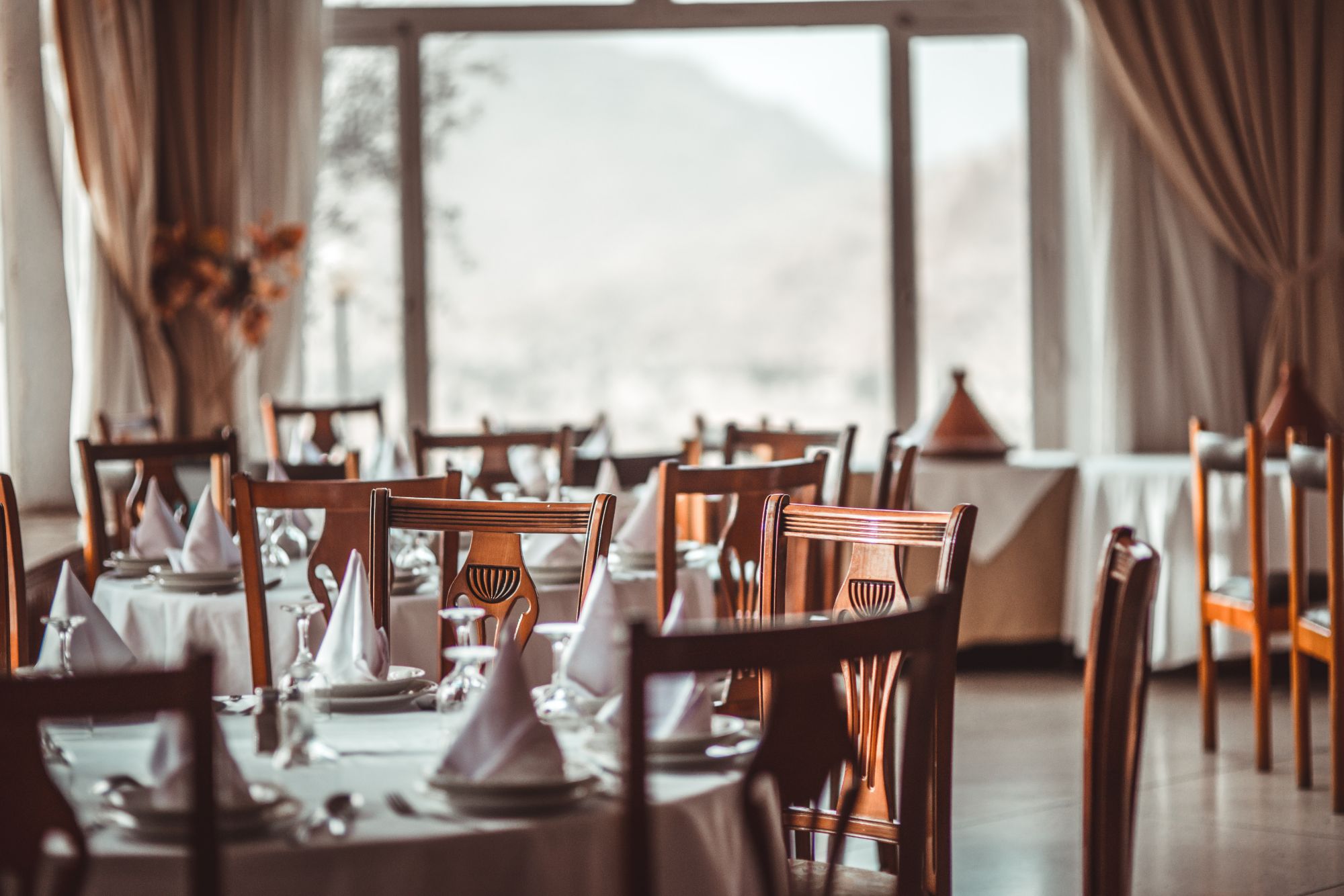 Elegancka restauracja z białymi obrusami, nakrytymi stołami i widokiem na góry przez okno.
