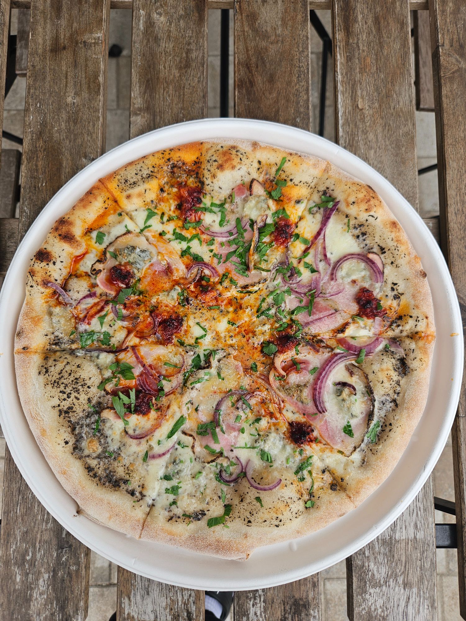 Pizza z serem, szynką, cebulą i ziołami na drewnianym stole.