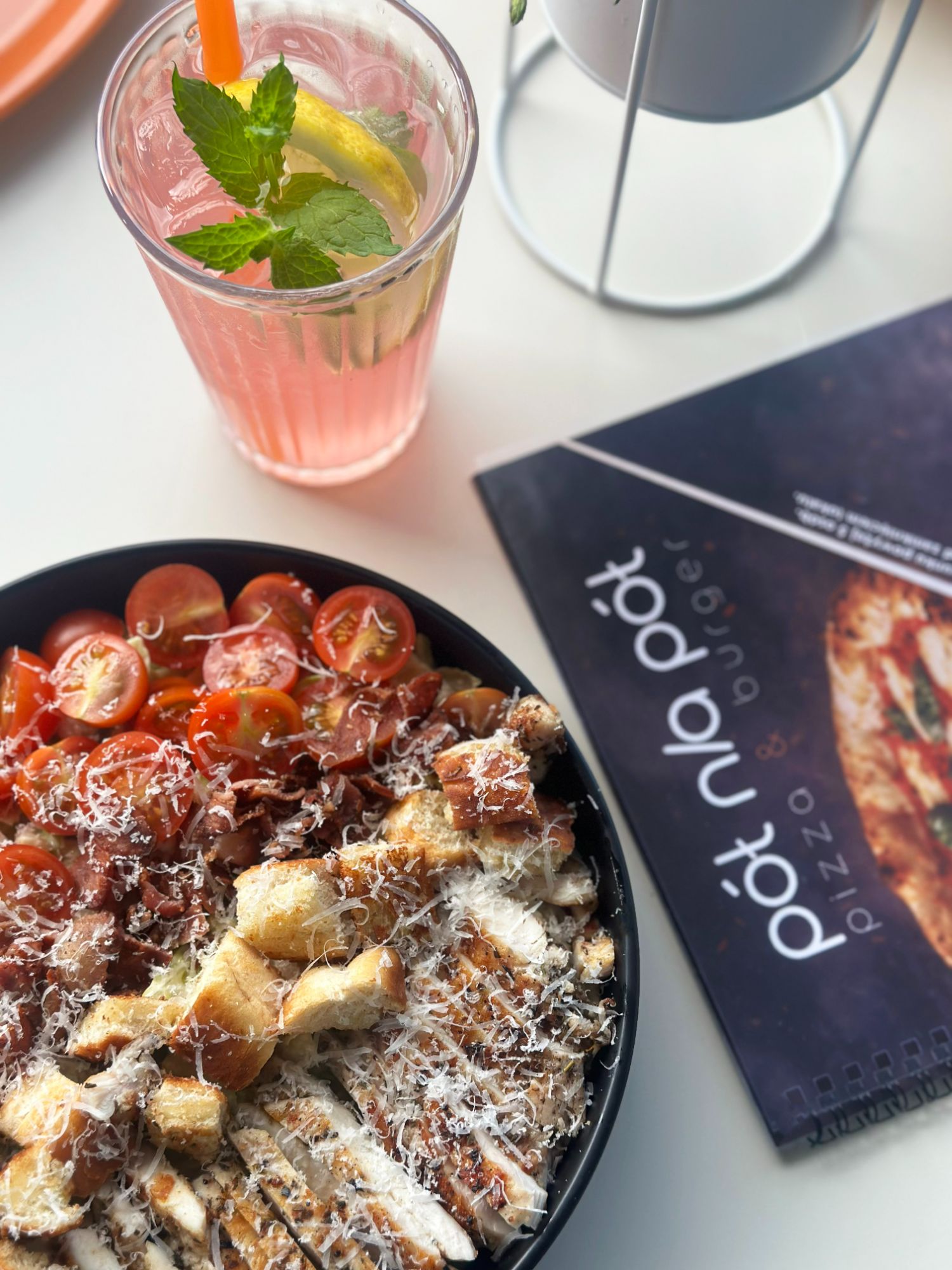 Sałatka z kurczakiem, pomidorkami i serem, obok napój owocowy i menu pizzerii.