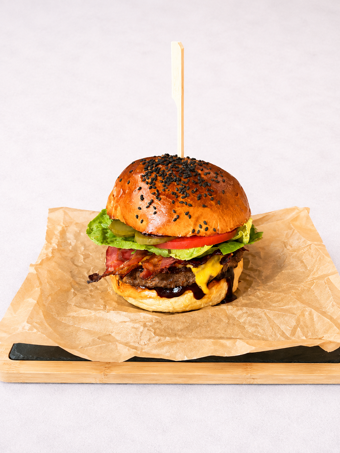 Soczysty hamburger z bekonem, serem cheddar, sałatą i pomidorem, podany na pergaminie na drewnianej desce.