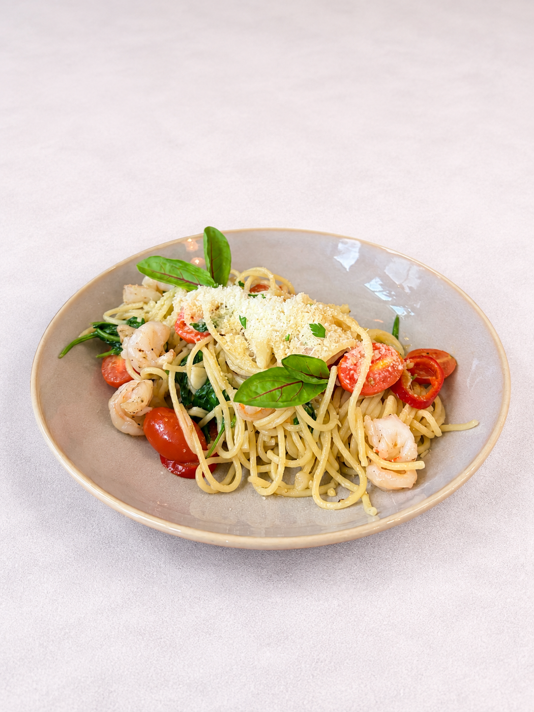 Makaron spaghetti z krewetkami, pomidorkami koktajlowymi, szpinakiem i serem na talerzu.