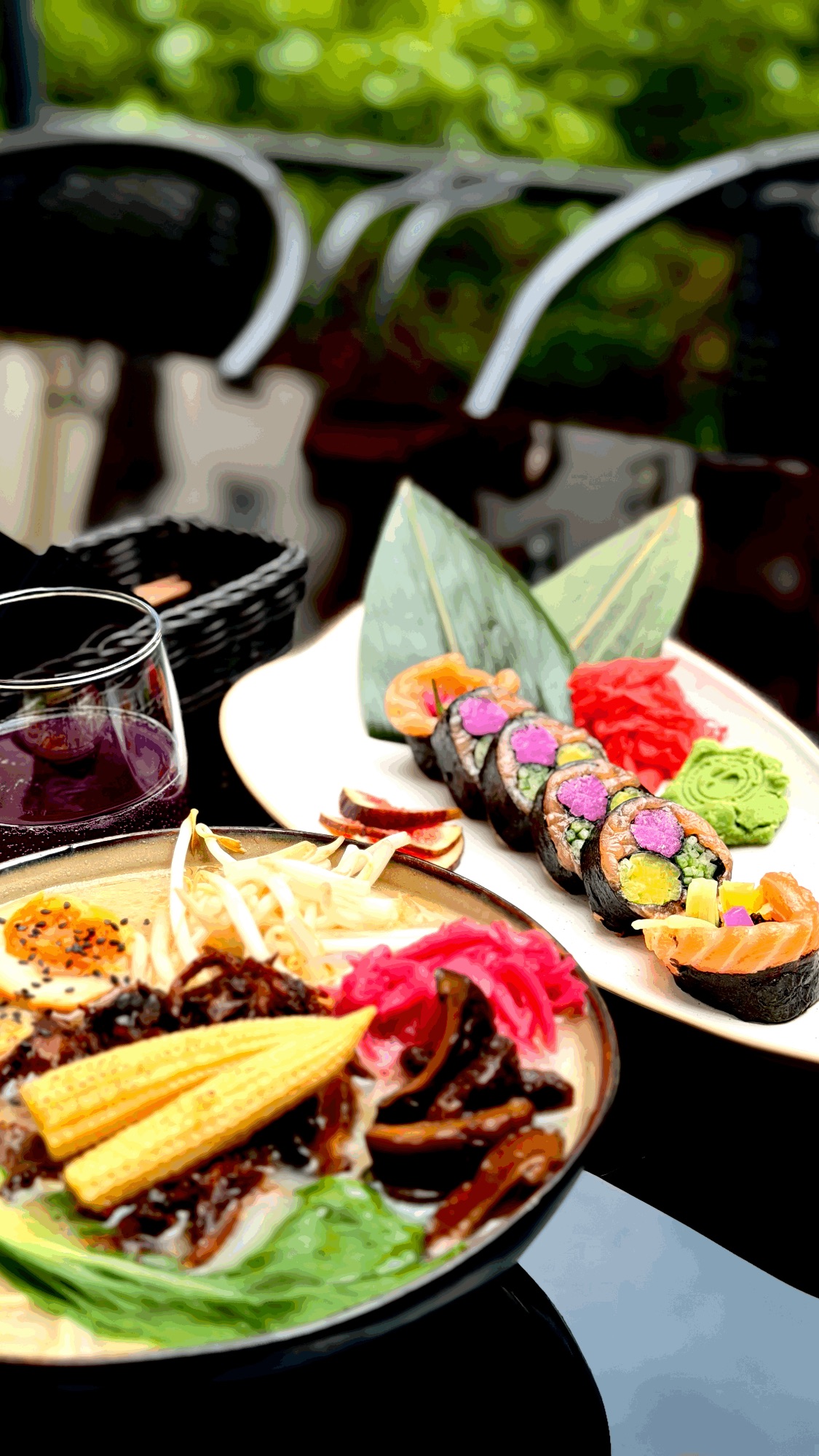 Kolacja z sushi, kolorową sałatką i warzywami, podana na tle zieleni.