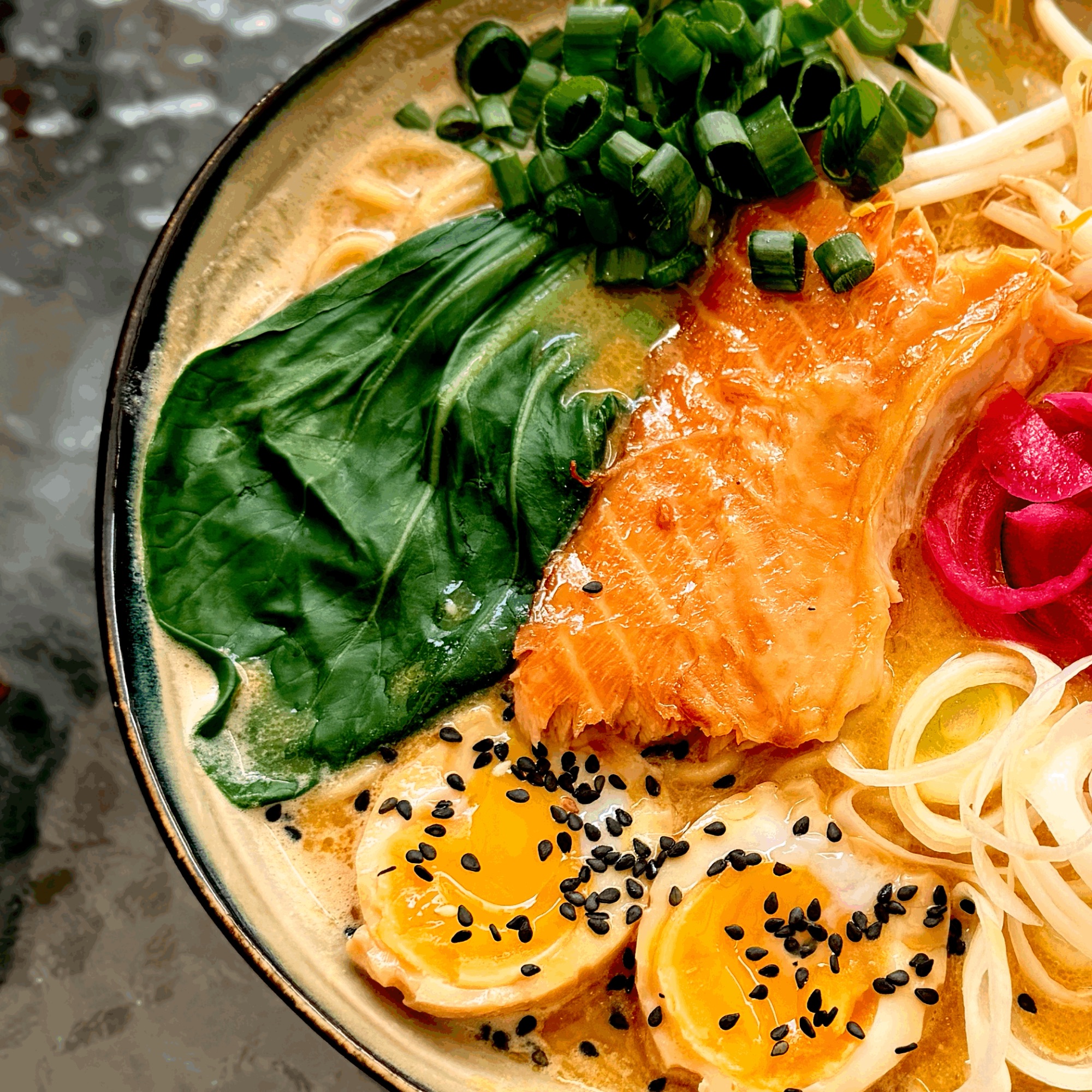 Zupa ramen z łososiem, jajkiem na twardo, świeżymi warzywami i dodatkiem cebulki dymki.