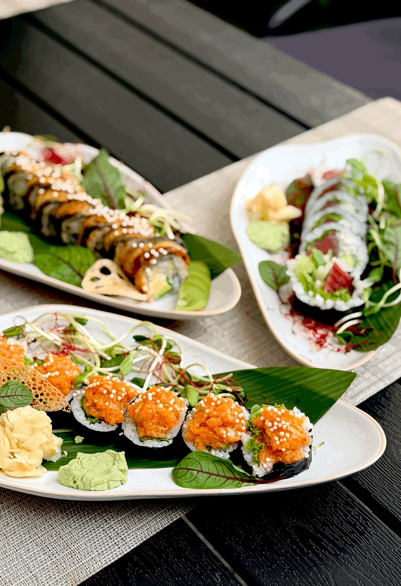Tradycyjne sushi na talerzach z wasabi, imbirem i świeżymi ziołami na tle drewnianego stołu.