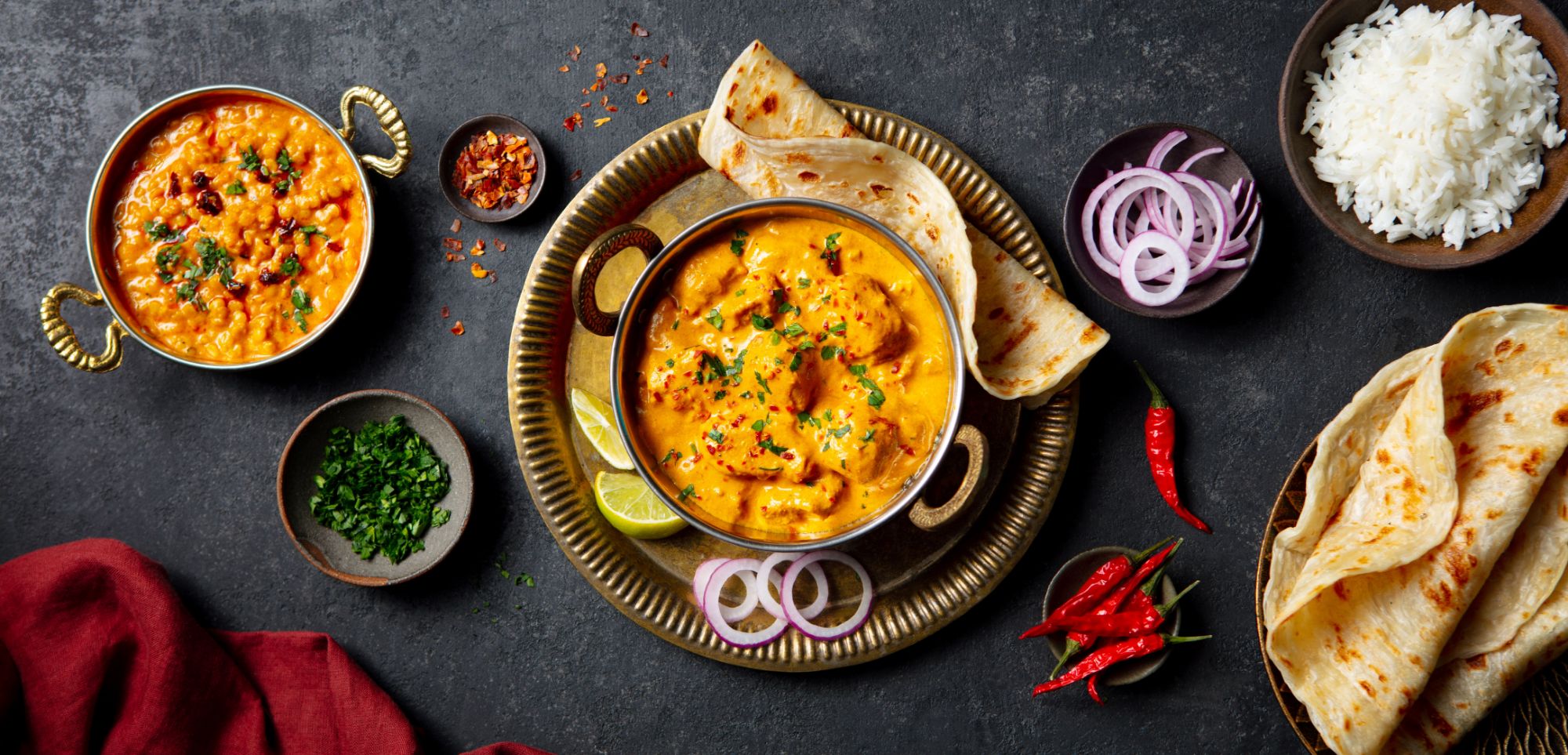 Kolacja z curry, ryżem, plackami naan, cebulą, zieloną pietruszką i czerwoną papryką na szarym tle.