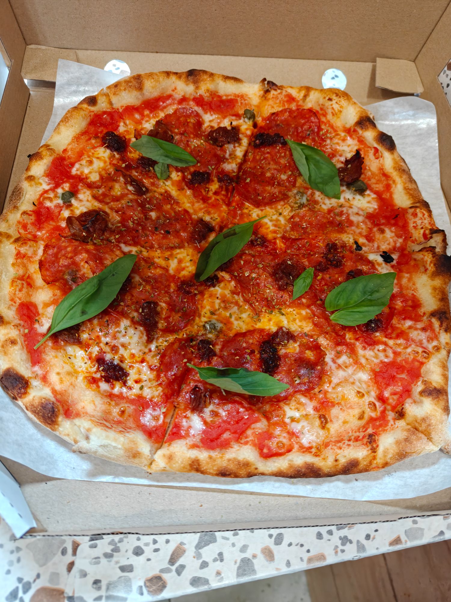 Pizza margherita z sosem pomidorowym, serem, suszonymi pomidorami i świeżą bazylią, w pudełku.