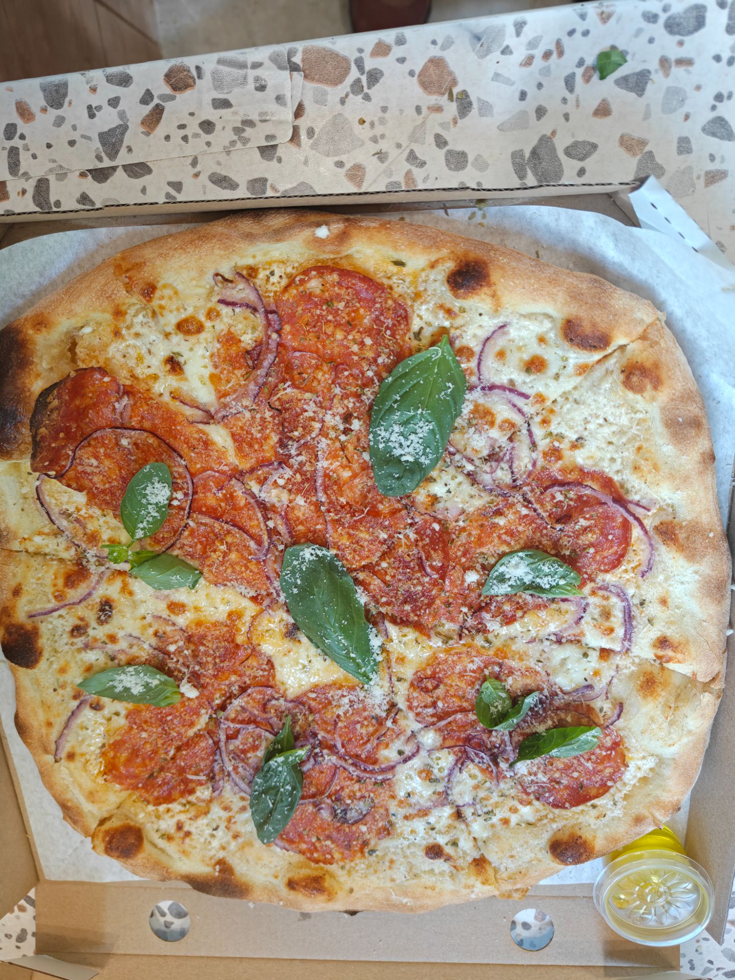 Pizza z salami, cebulą i bazylią, posypana parmezanem, podana w pudełku.