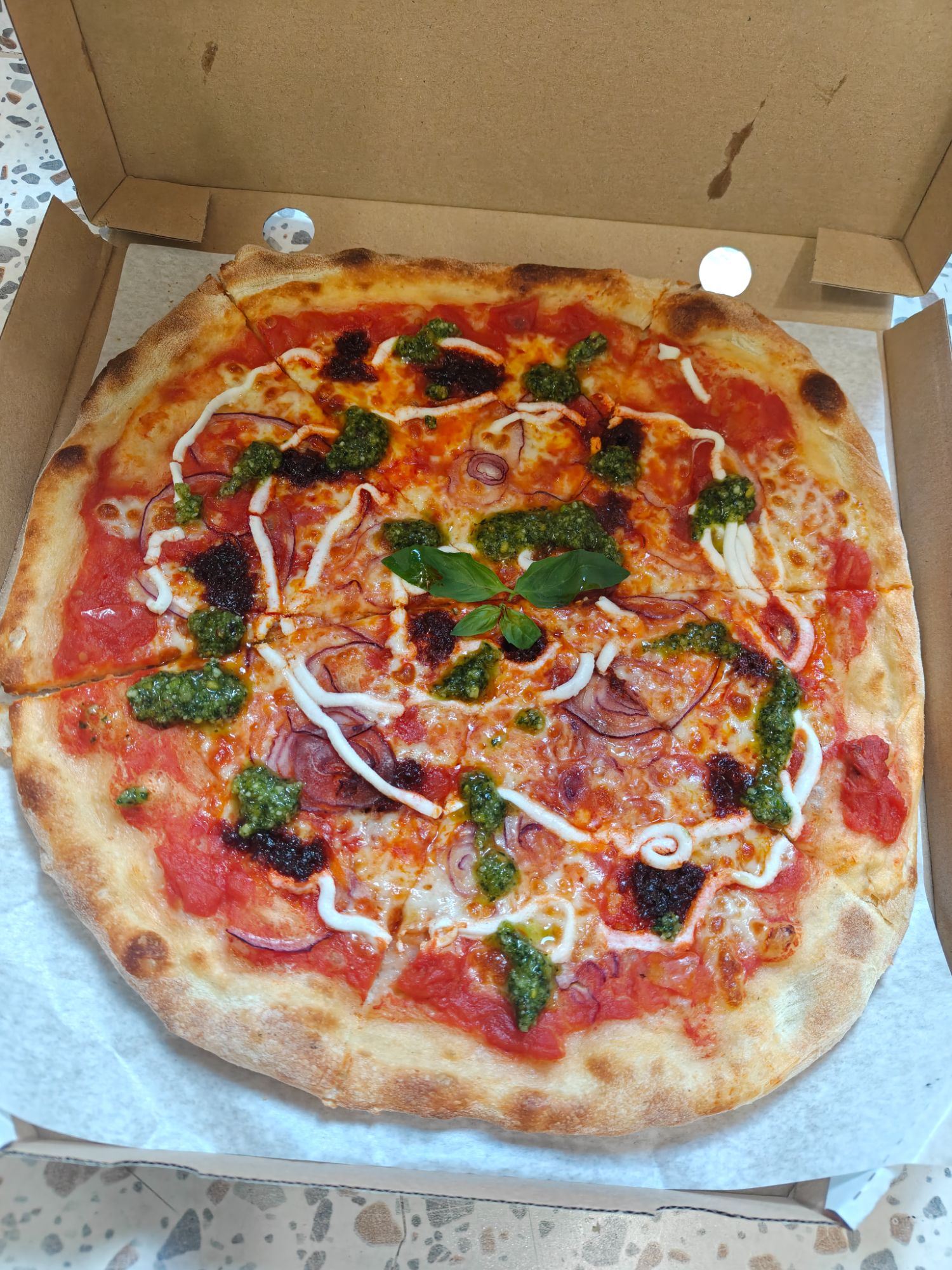 Pizza z sosem pomidorowym, serem, bazylią i ziołowym pesto w opakowaniu.