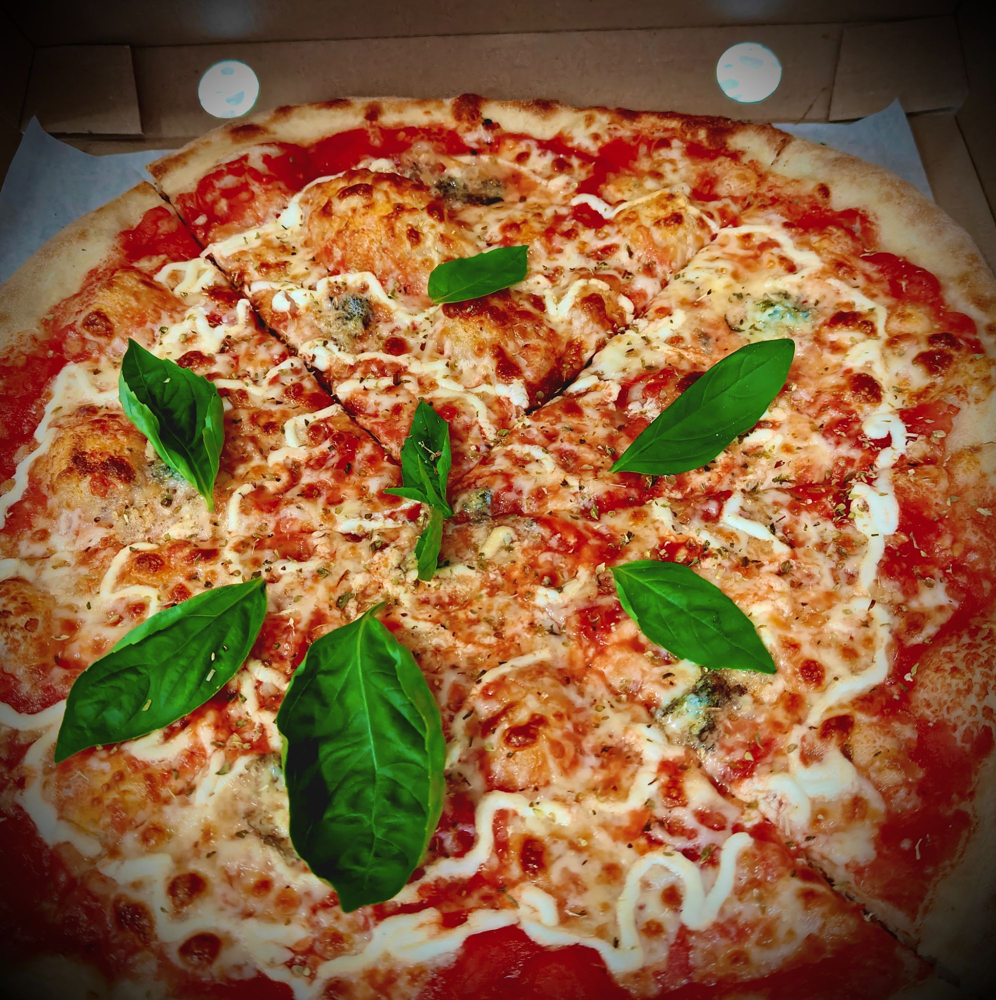 Pizza Margherita z sosem pomidorowym, serem mozzarella i świeżą bazylią w kartonowym pudełku.