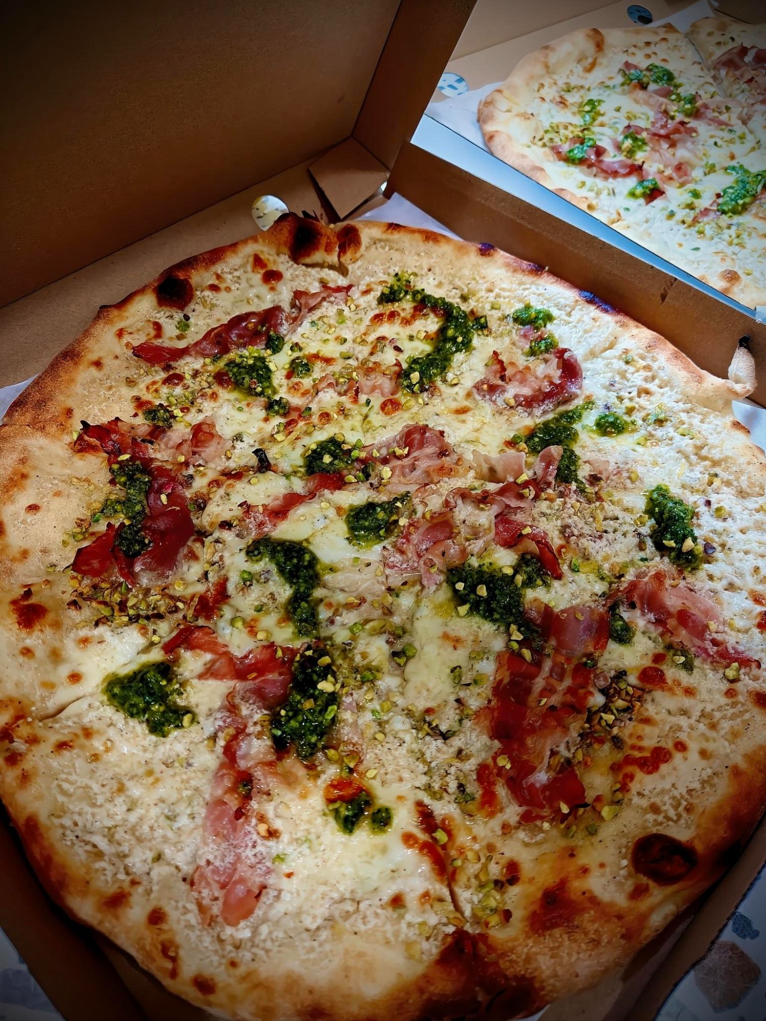 Pizza z serem, pesto, szynką parmeńską i posypką, podana w otwartym pudełku.