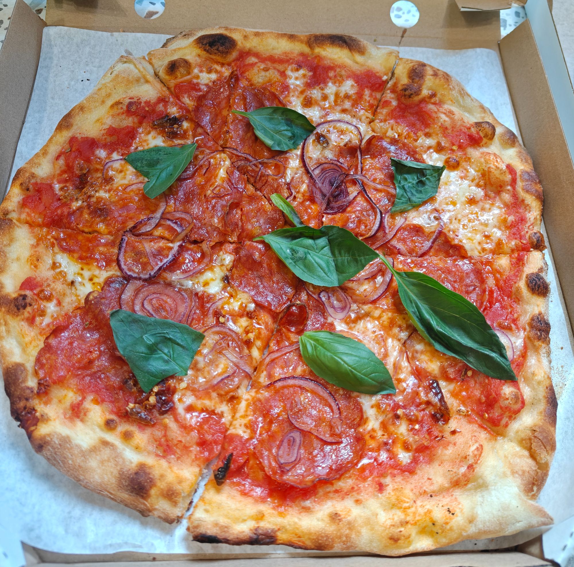 Pizza z sosem pomidorowym, serem, cebulą czerwoną i świeżą bazylią, w kartonowym pudełku.