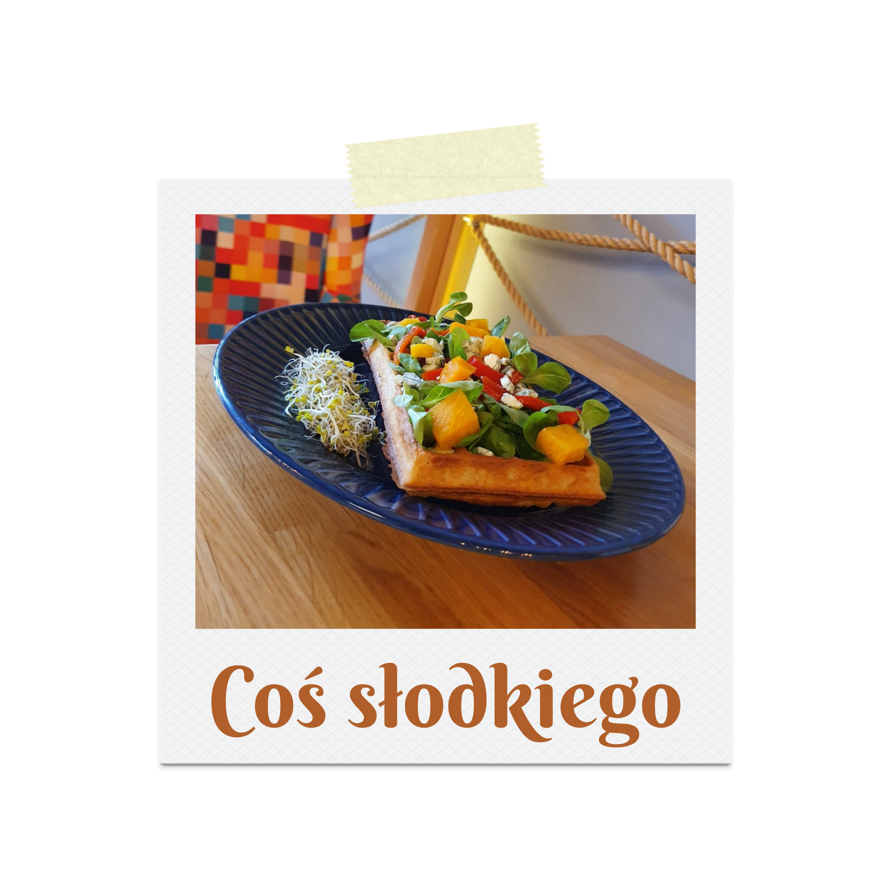 Wafel z warzywami, kiełkami i owocami na niebieskim talerzu, z napisem "Coś słodkiego".