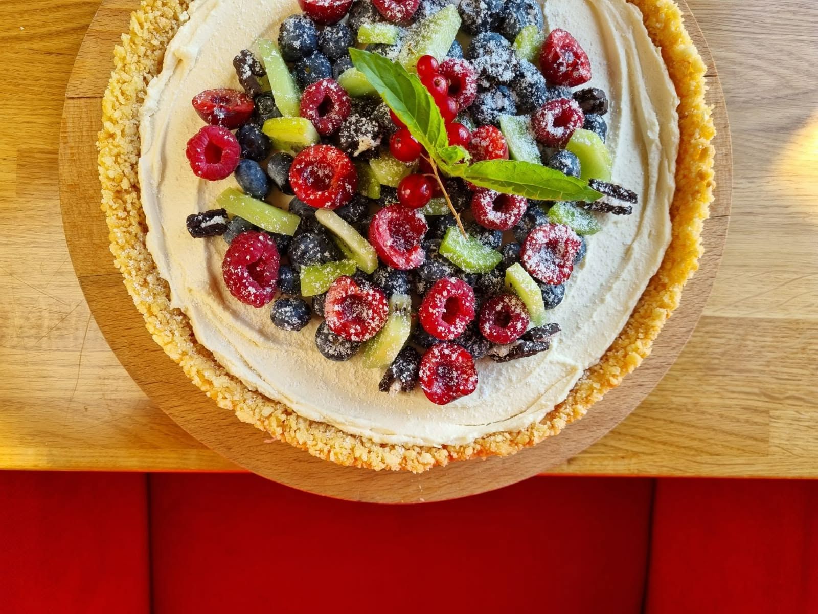 Tarta z kremem, owocami leśnymi i ozdobami z mięty na drewnianym talerzu.