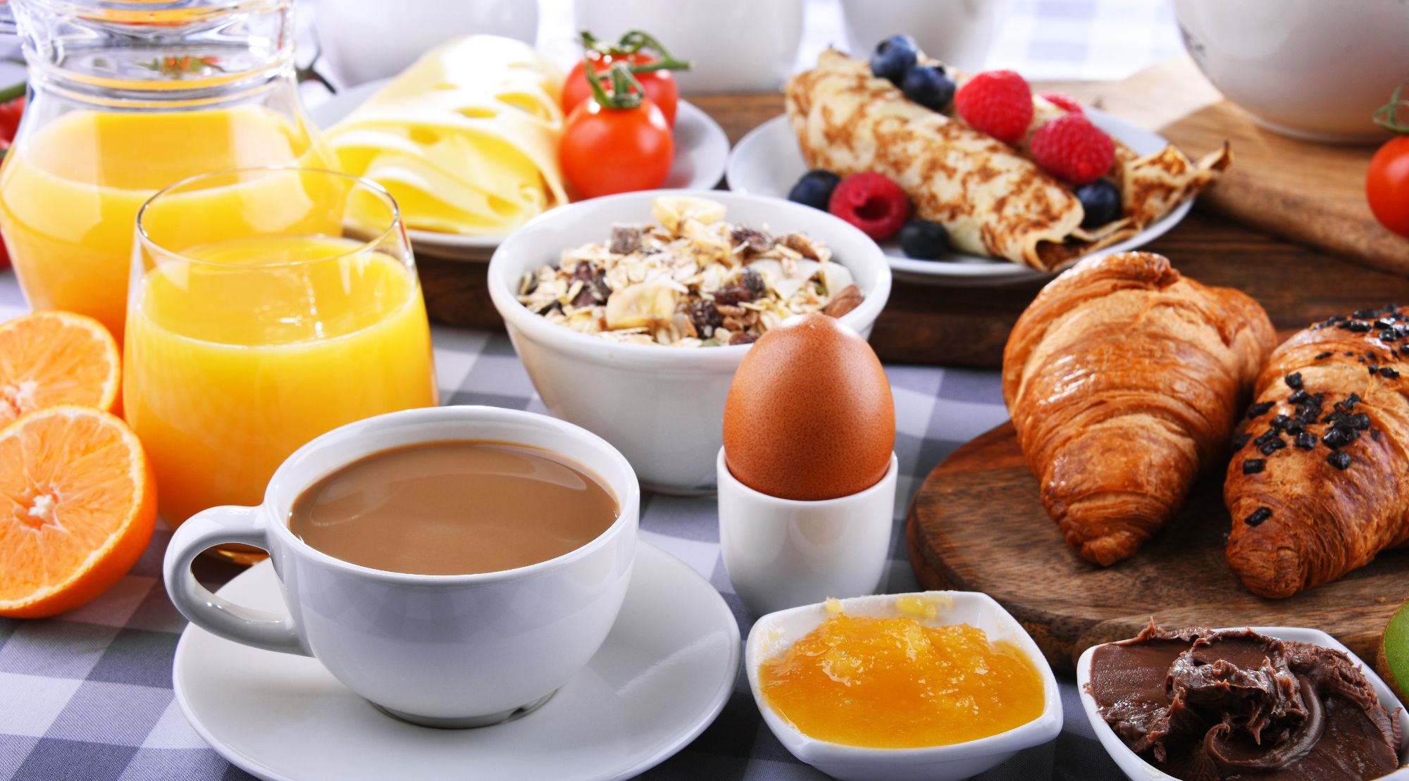 Śniadanie z kawą, sokiem pomarańczowym, croissantem, jajkiem na twardo, naleśnikami i owocami na stole.