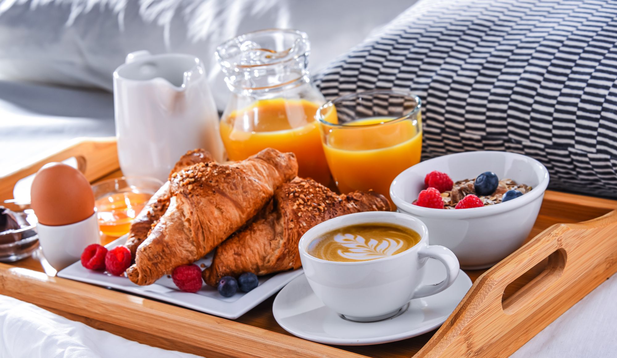 Śniadanie w łóżku: rogaliki, kawa, świeżo wyciśnięty sok, jogurt z owocami, jajko na twardo.