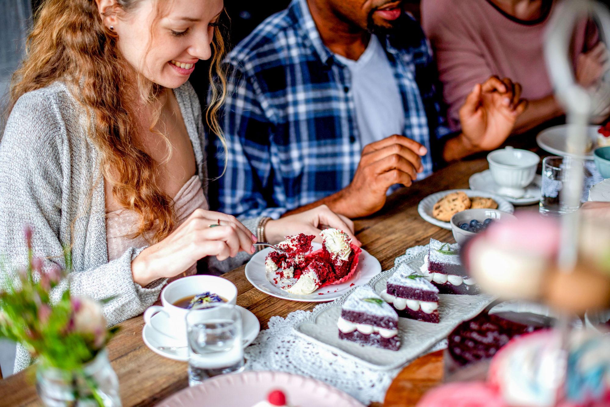 Grupa przyjaciół cieszy się deserami, na stole ciasto red velvet i filiżanki kawy.