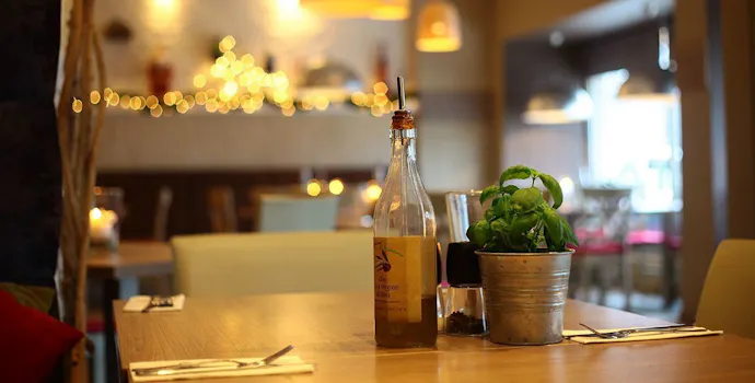 Stół w restauracji z butelką oliwy, doniczką bazylii i przytulnym oświetleniem w tle.