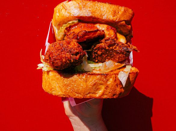 Burgery z kurczakiem, sałatą i odpowiednimi sosami na tle czerwonej ściany.