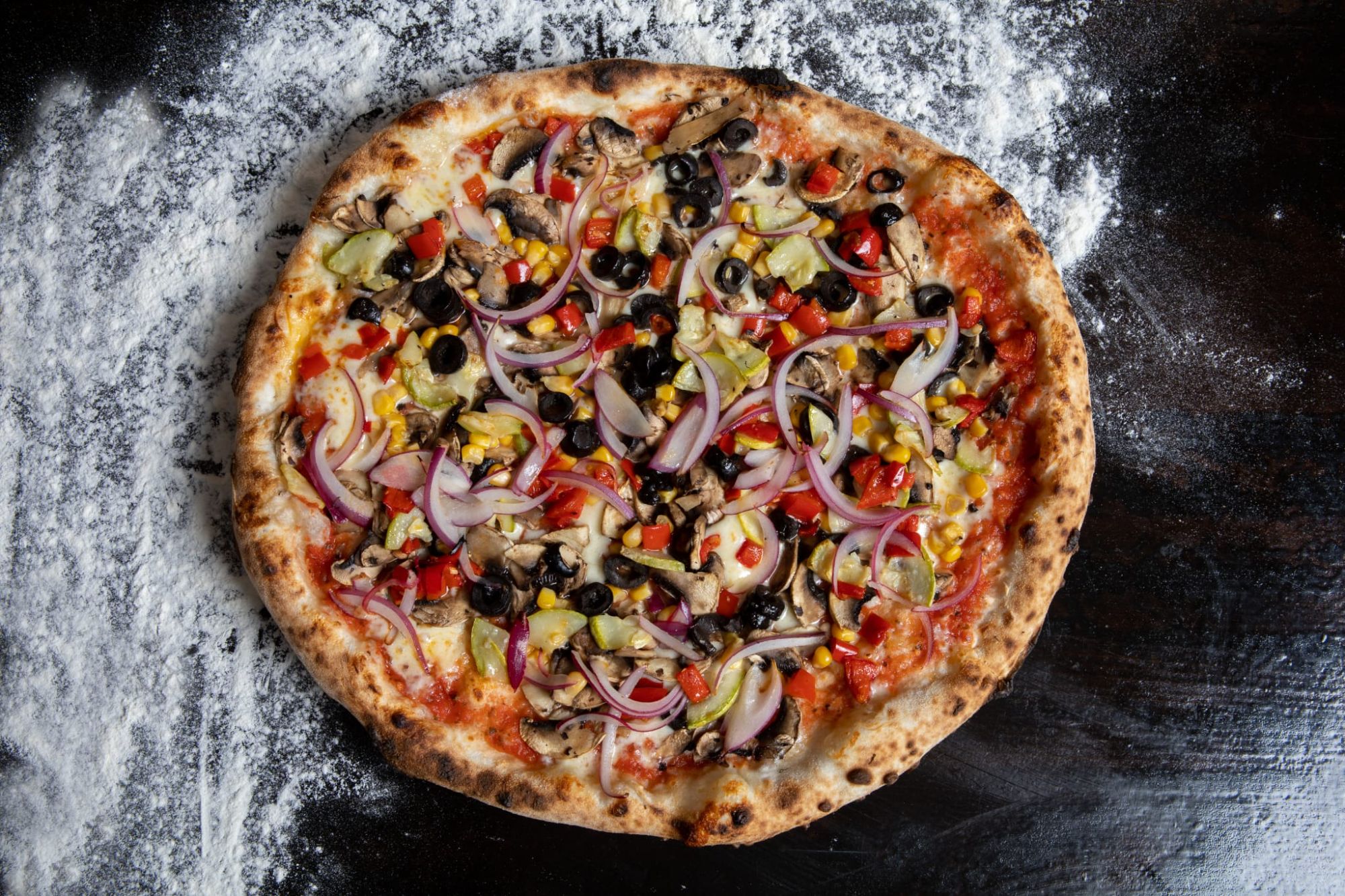 Pizza cu legume colorate, inclusiv ciuperci, măsline, ardei și ceapă, pe o bază crocantă.