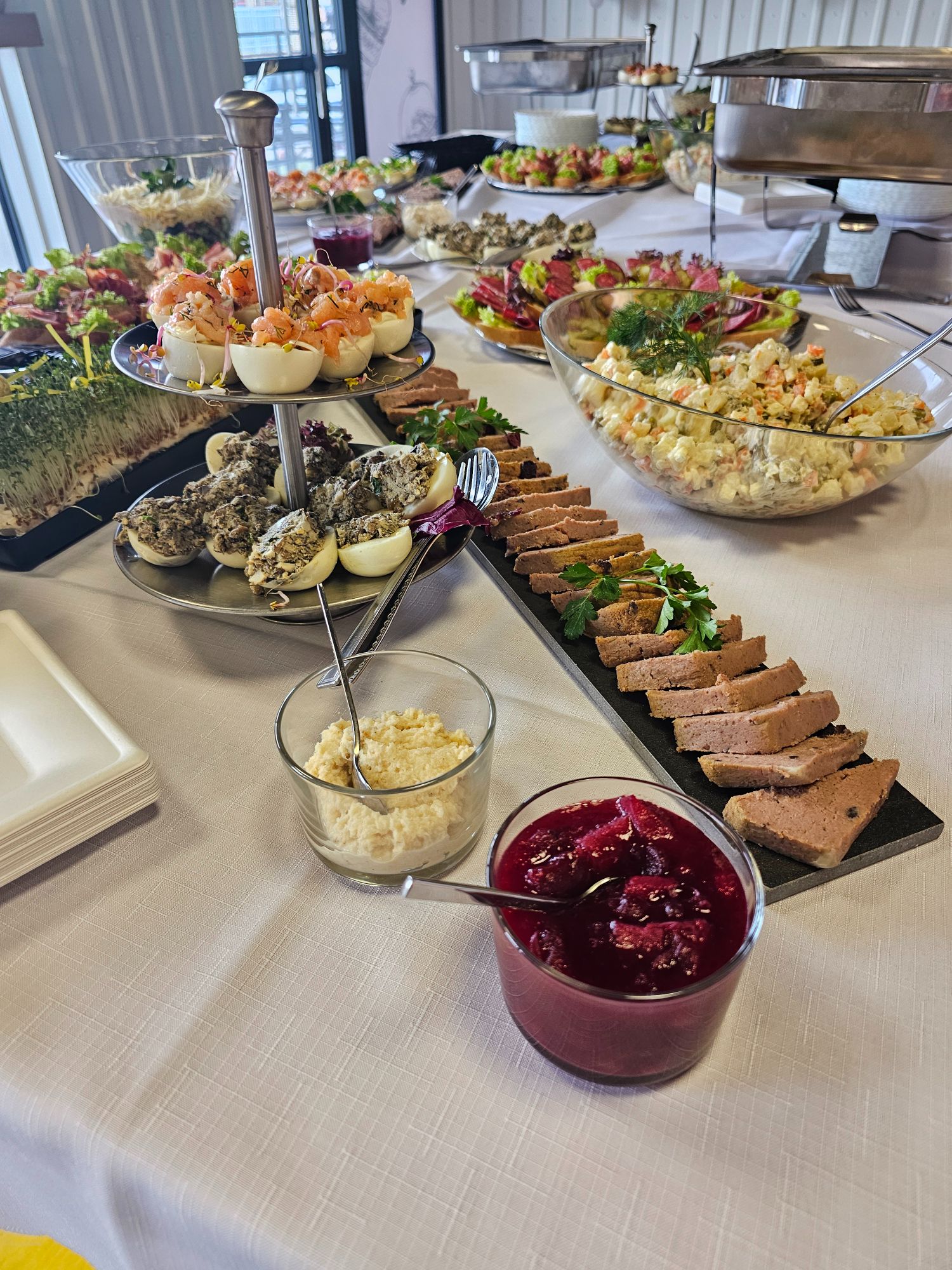 Rozmaite potrawy na bufecie: sałatki, przystawki, jajka, świeże owoce oraz sosy w eleganckich naczyniach.