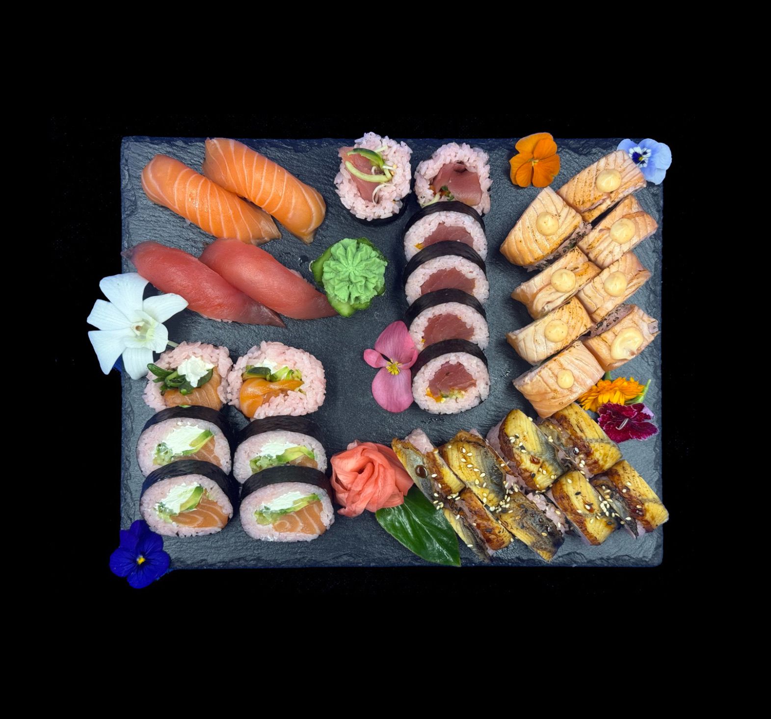 Różnorodne sushi na czarnym tle: łososie, nigiri, maki i dekoracyjne kwiaty.