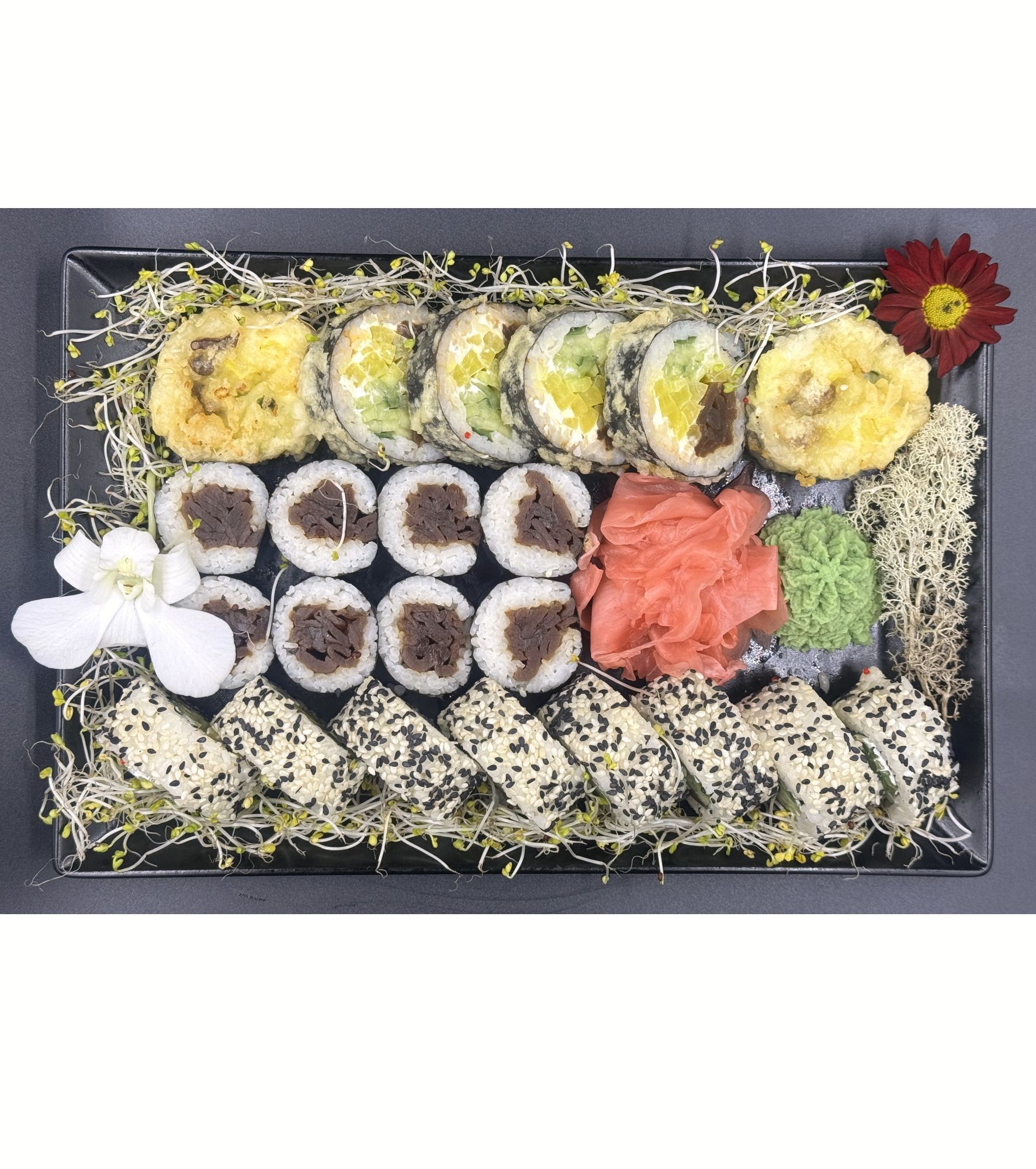 Talerz różnorodnych sushi: rolki ryżowe z surową rybą, awokado, wasabi i marynowanym imbirem, udekorowane świeżymi kwiatami.