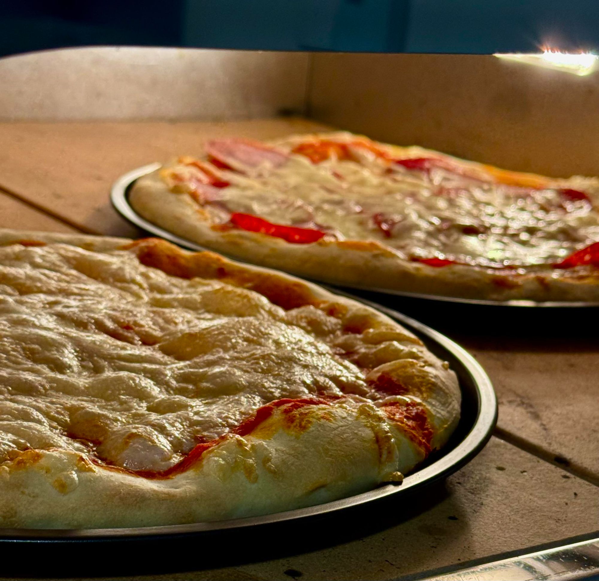 Dwie pizze na okrągłych blaszkach, wypieczone z serem, pomidorami i przyprawami, w piecu na kamieniu.