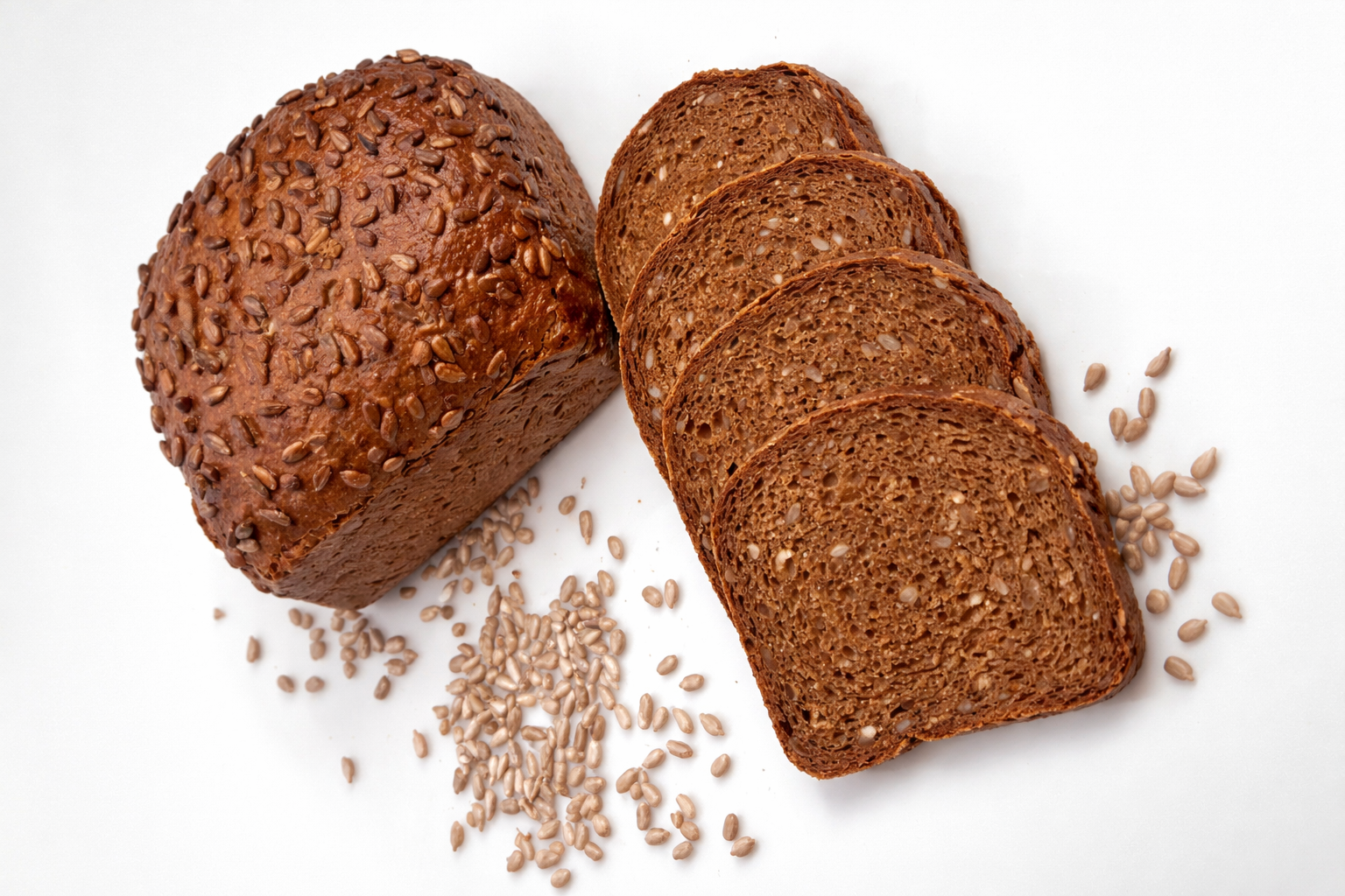 Bochenek chleba żytniego z ziarnami słonecznika oraz pokrojone na plasterki kromki leżące obok.