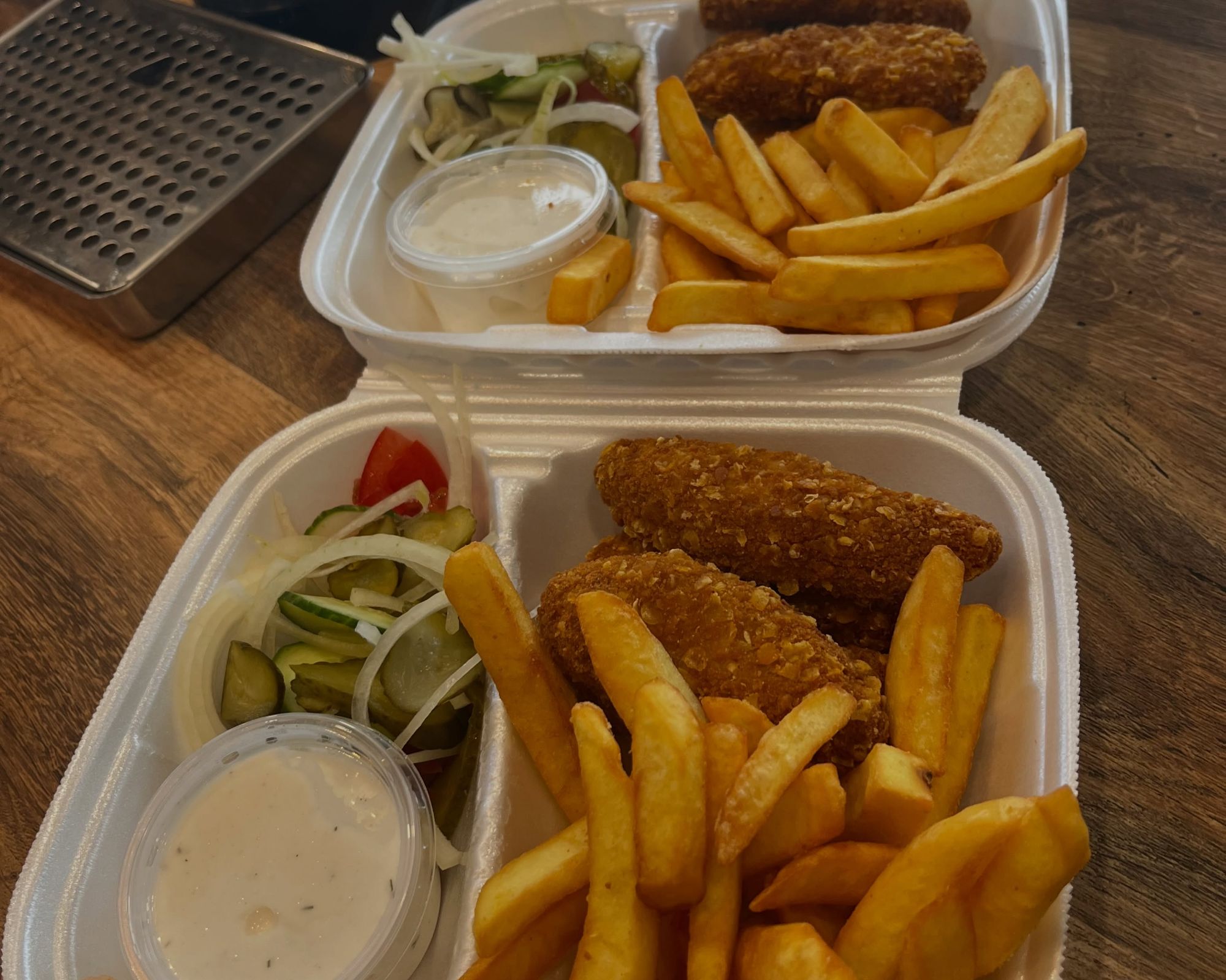 Frytki, nuggetsy i sałatka podane w plastikowych pojemnikach.