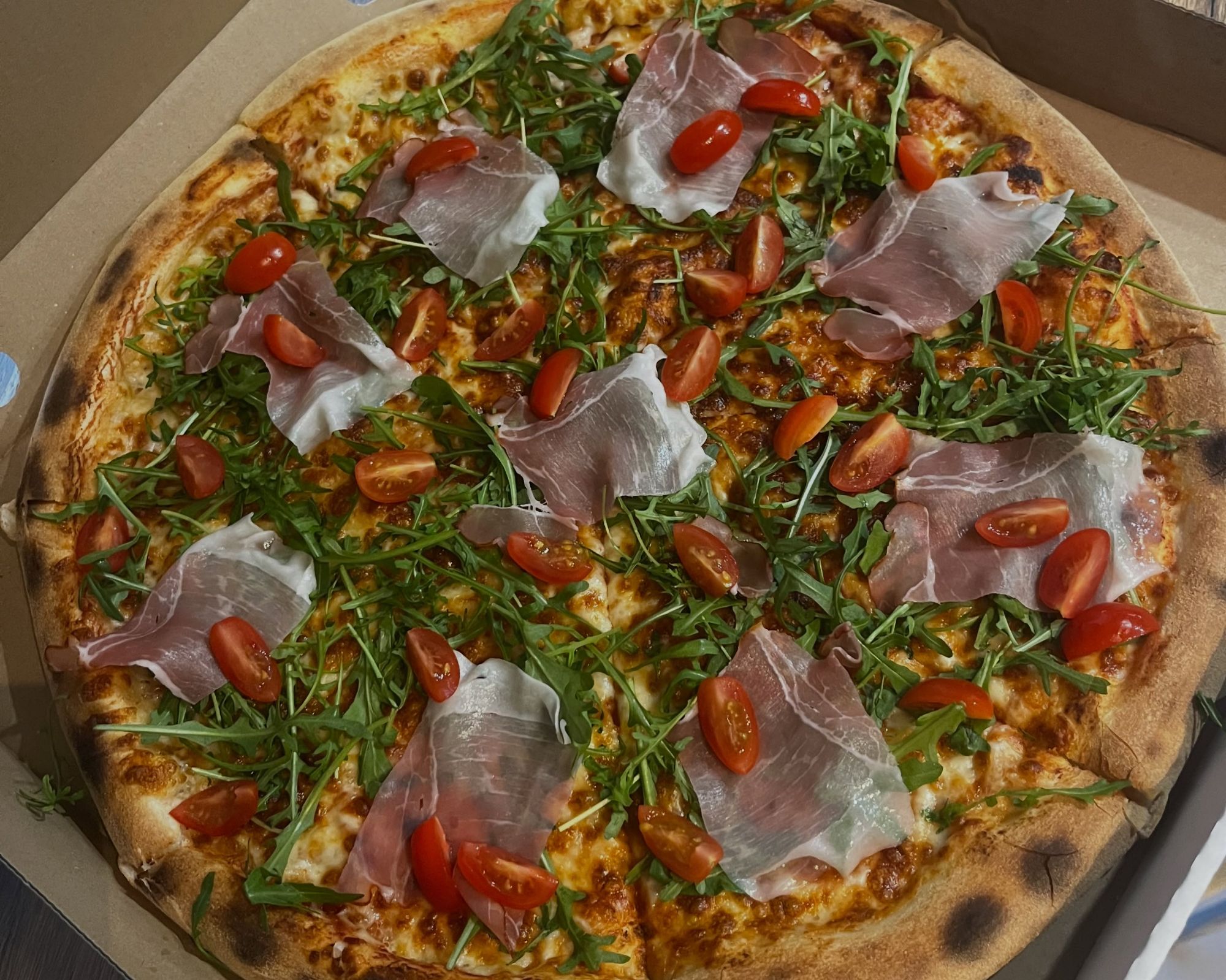 Pizza z rukolą, pomidorkami koktajlowymi i szynką parmeńską na chrupiącym cieście.