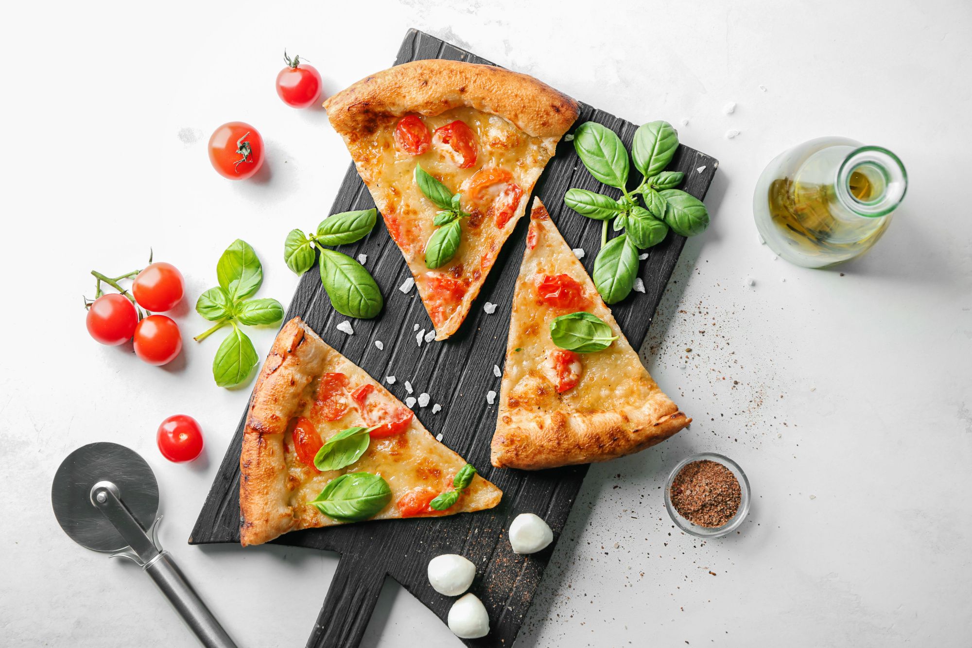 Trzy kawałki pizzy z sosem pomidorowym, bazylią i serem mozzarella, otoczone pomidorkami i oliwą.