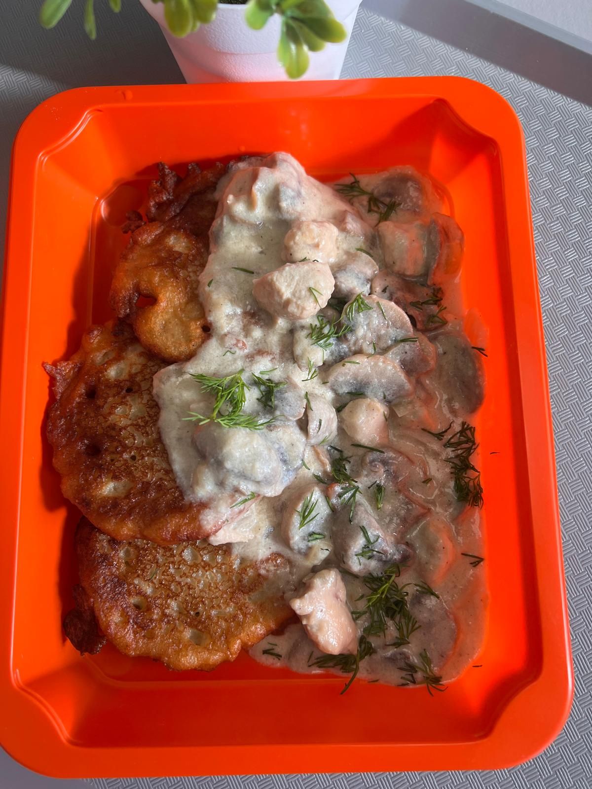Placuszki ziemniaczane z sosem na bazie grzybów i kurczaka, podane na pomarańczowym talerzu.